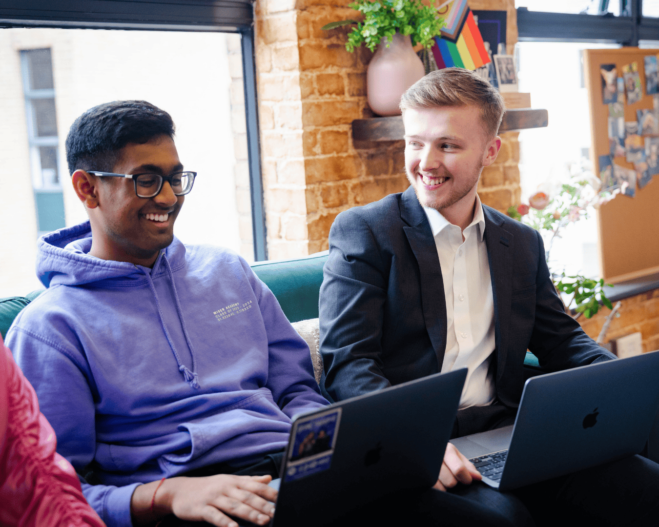 Two males laughing sat on a sofa with laptops