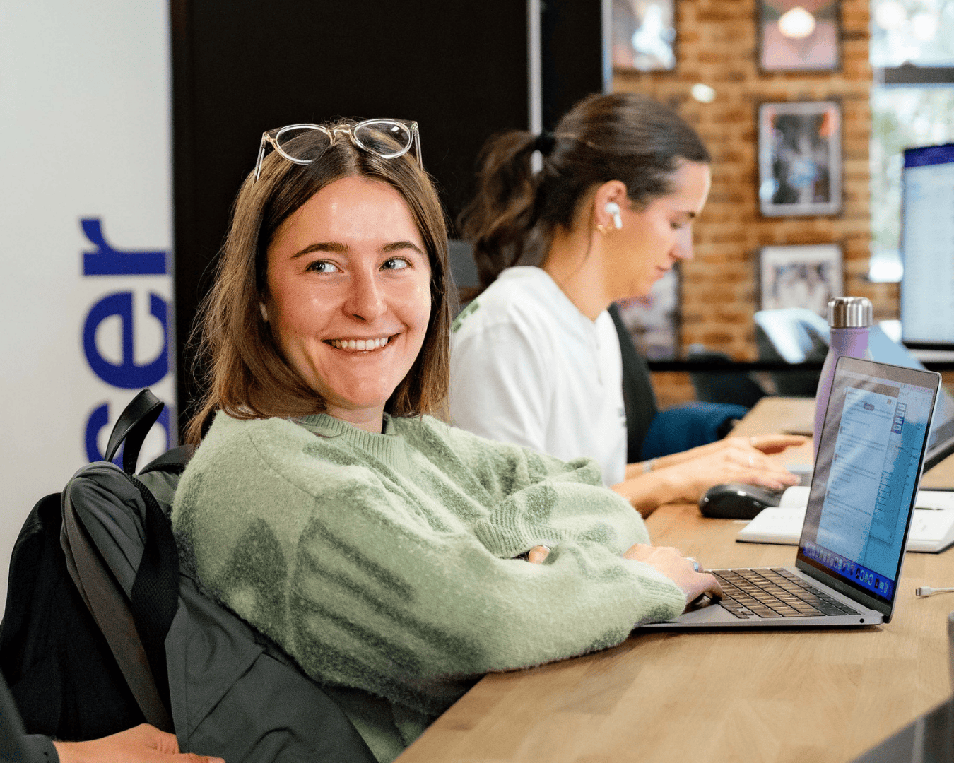 female with brown hair sat at a desk smiling