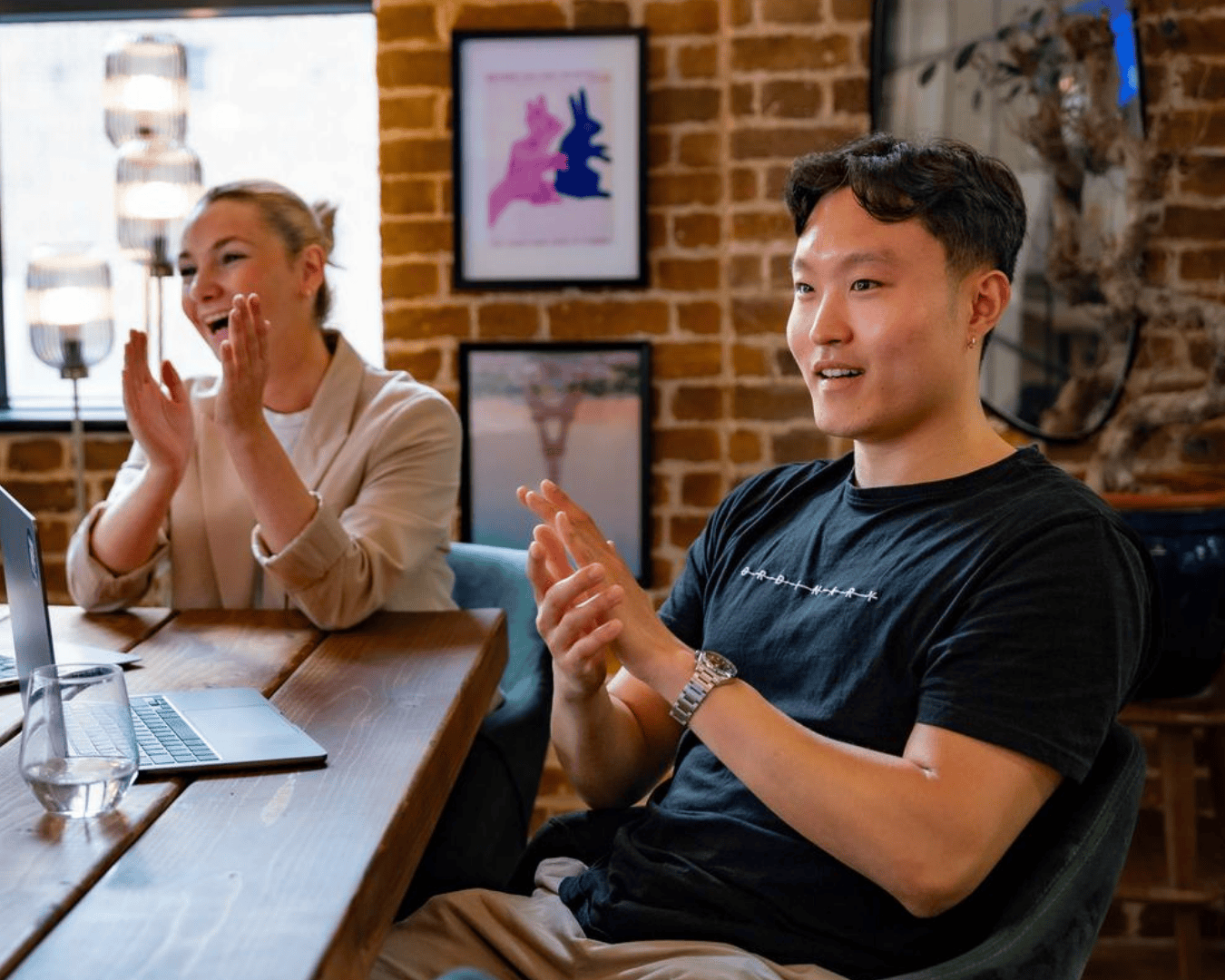Photo of male and female clapping in a meeting room with exposed brick walls