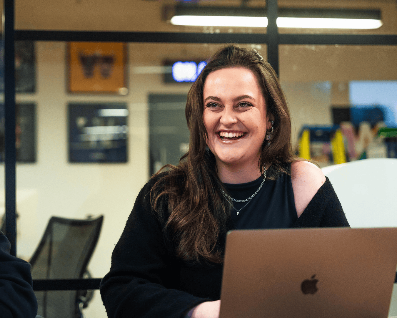 Photo of female with brown hair laughing with a laptop in front of her