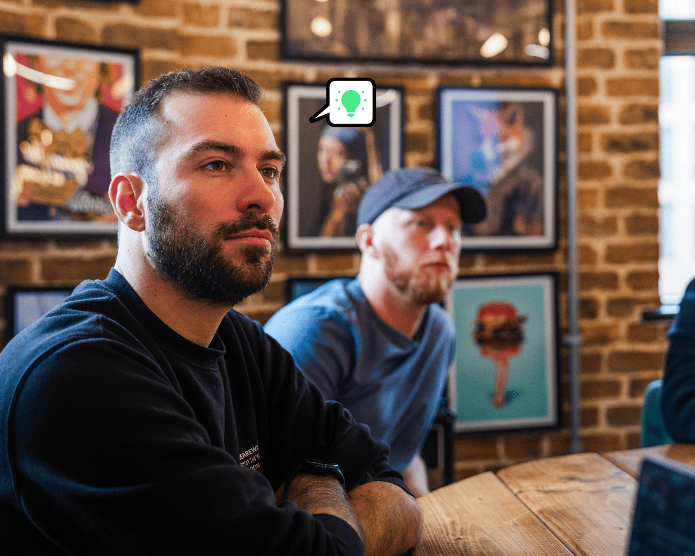 Photo of two males looking at a screen with a frames behind them on an exposed brick wall