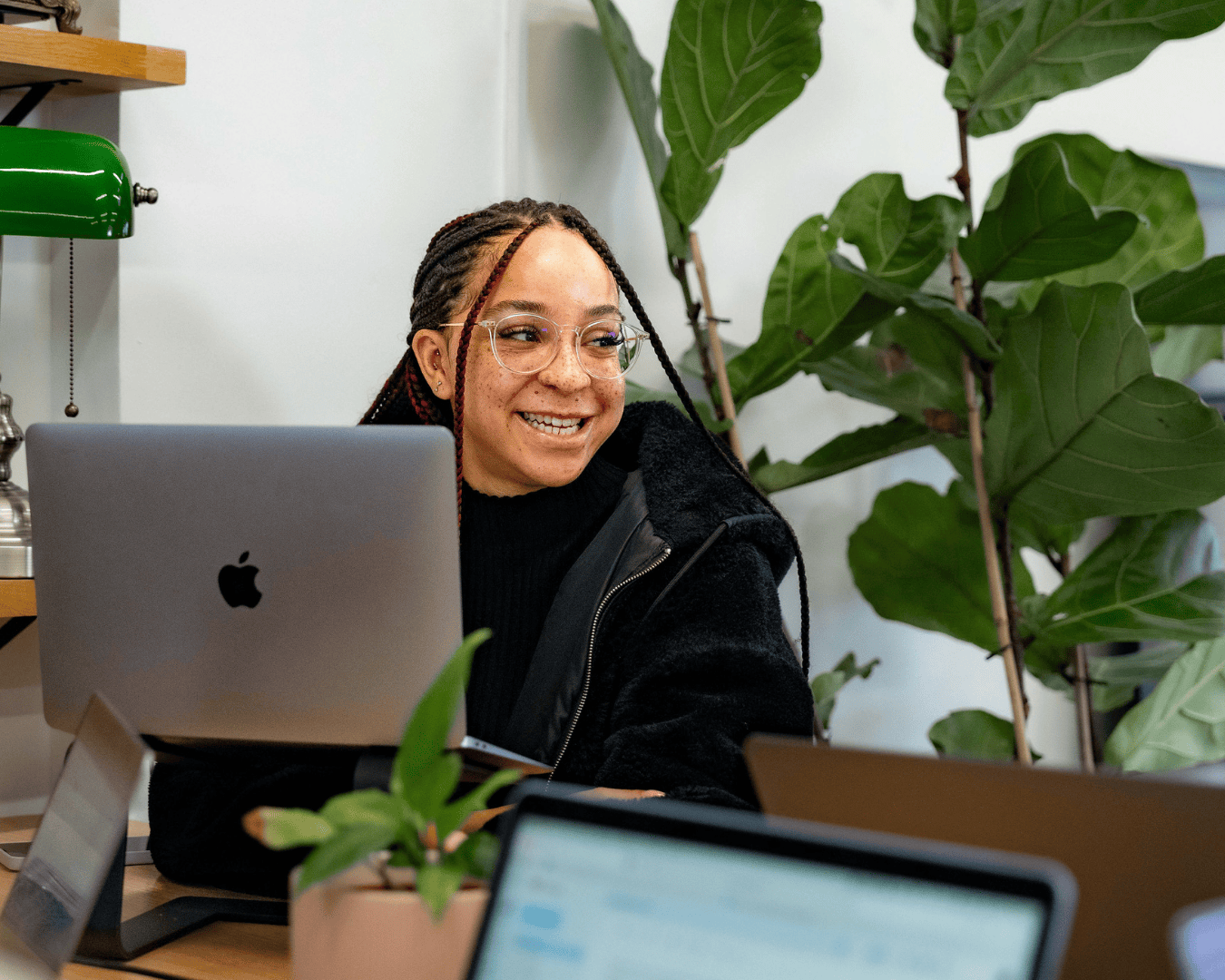 Photo of female smiling at her desk with plants behind her