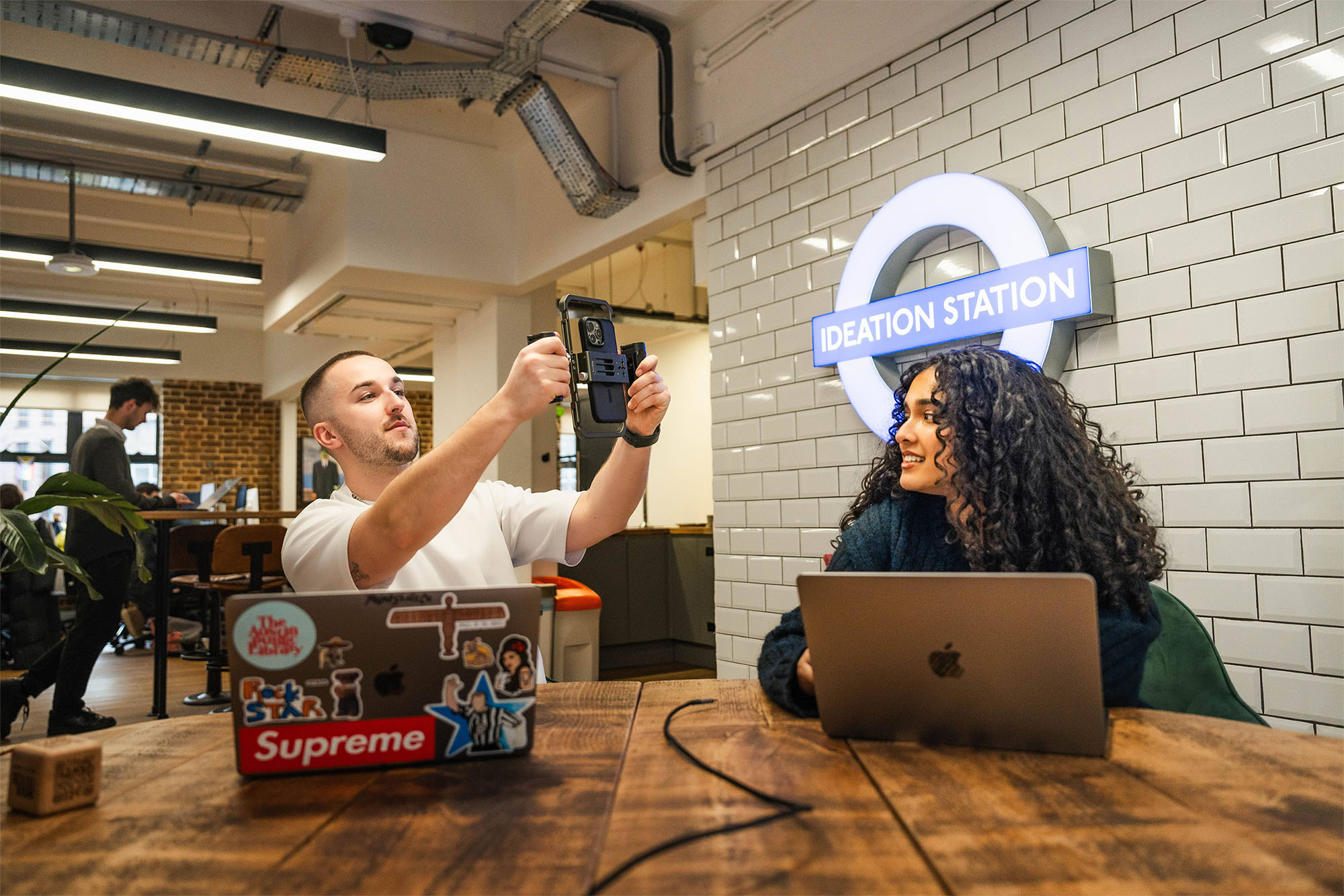 Our social media team, a white man with close cropped short hair, and an indian woman with long brown curly hair, are both in their twenties. They're workshopping some social media ideas together using iPhones and a whiteboard.