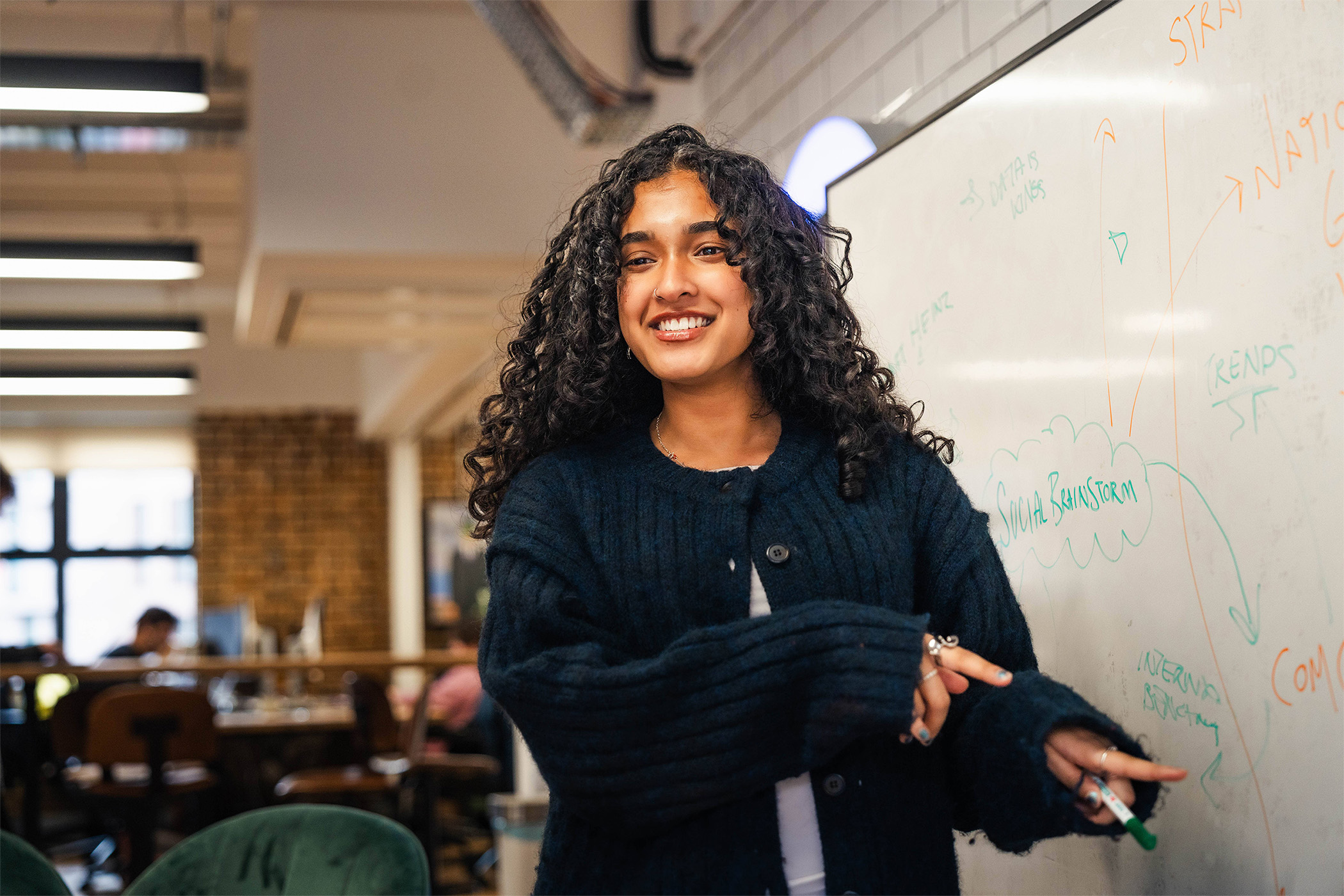 Our social media team, a white man with close cropped short hair, and an indian woman with long brown curly hair, are both in their twenties. They're workshopping some social media ideas together using iPhones and a whiteboard.