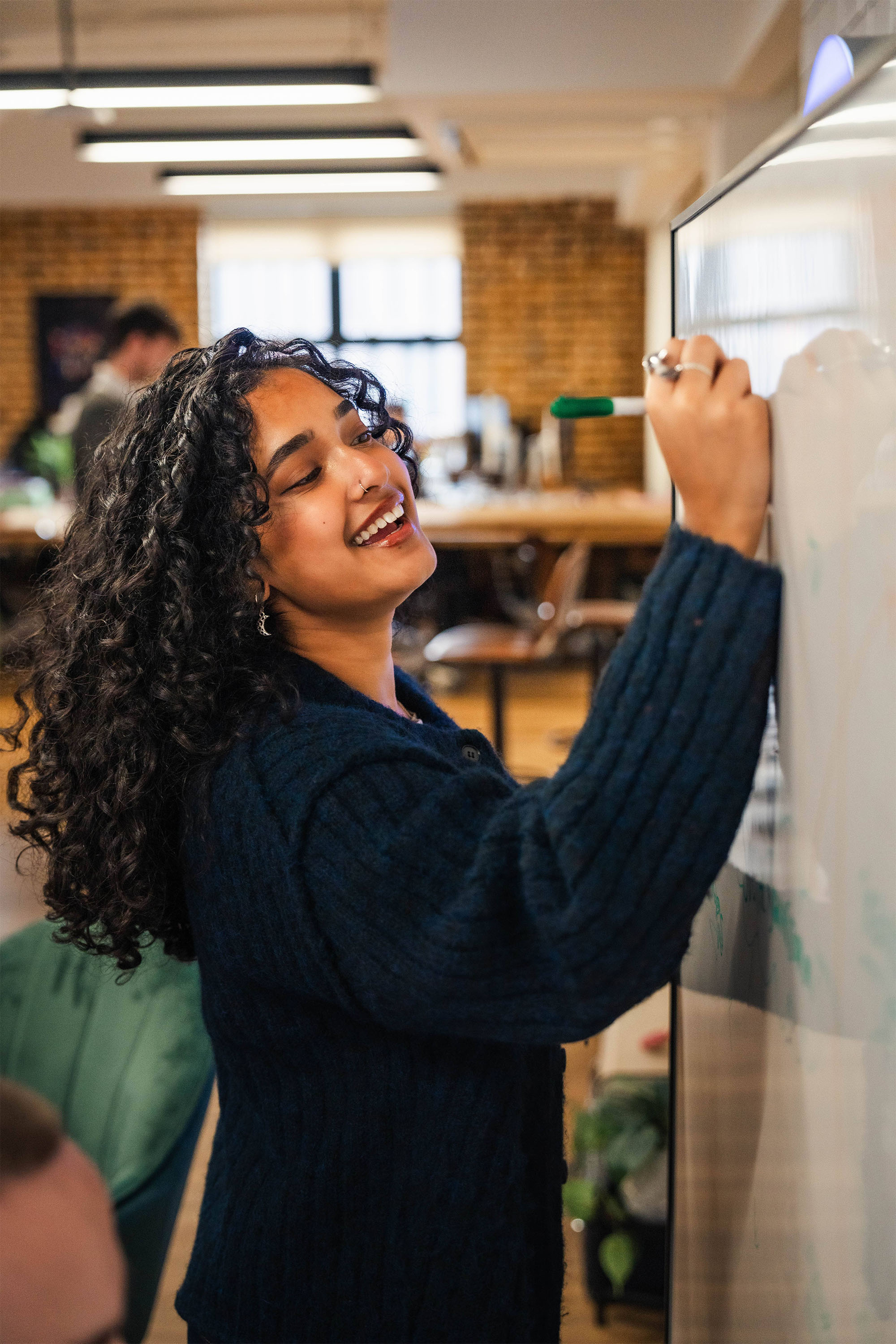 Our social media team, a white man with close cropped short hair, and an indian woman with long brown curly hair, are both in their twenties. They're workshopping some social media ideas together using iPhones and a whiteboard.