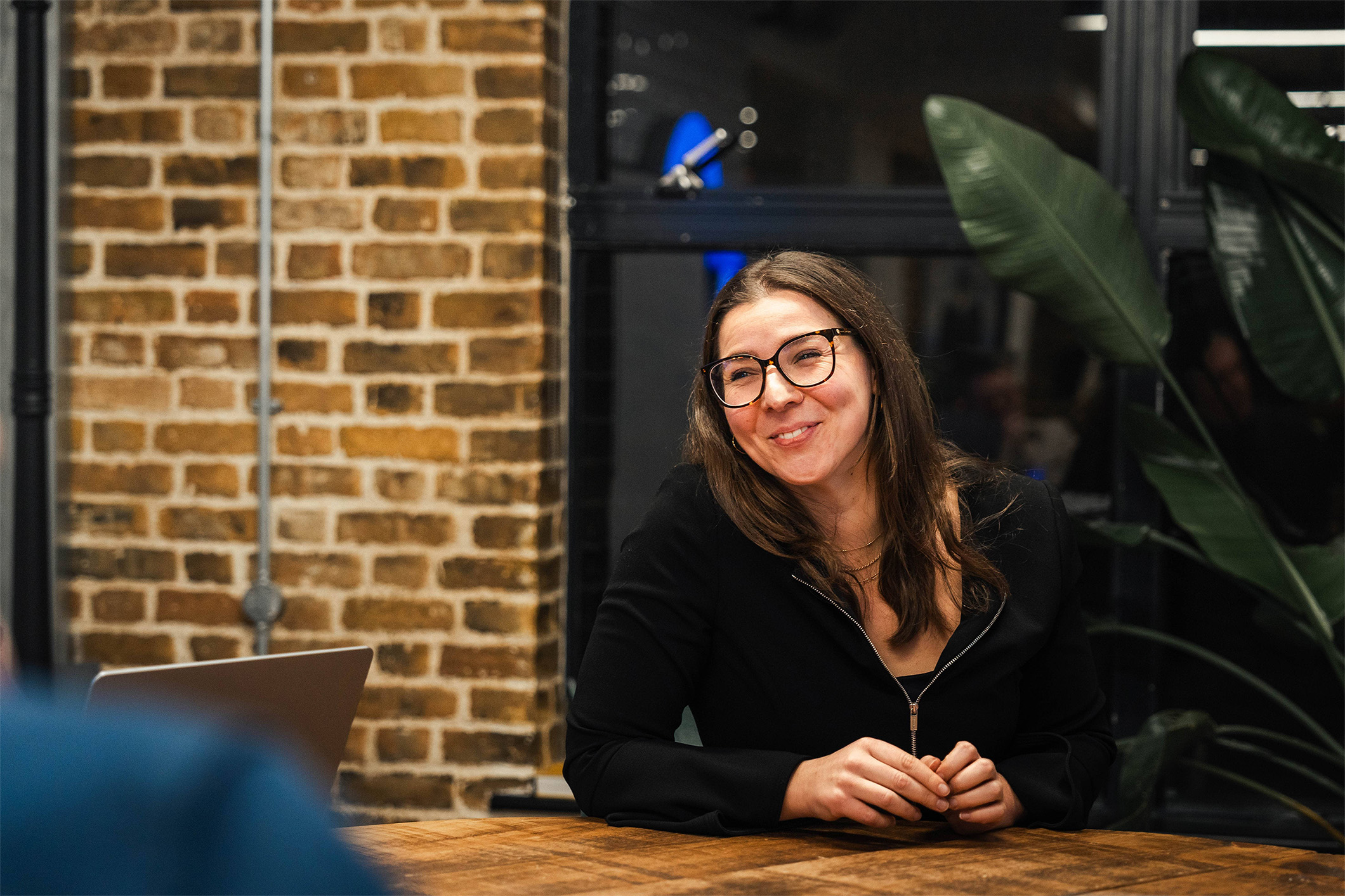 photo of female with brown hair smiling in a meeting, wearing a black jumper and glasses