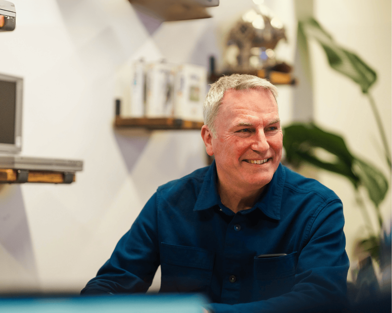 Photo of man with grey hair wearing a blue shirt smiling looking away from the camera