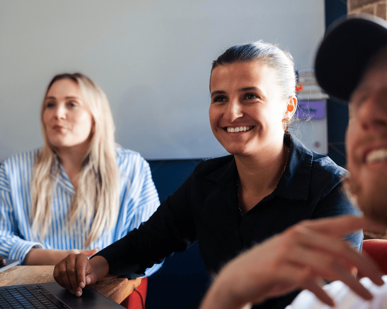 Three colleagues engaged in a meeting, smiling and listening, in a bright, modern office setting