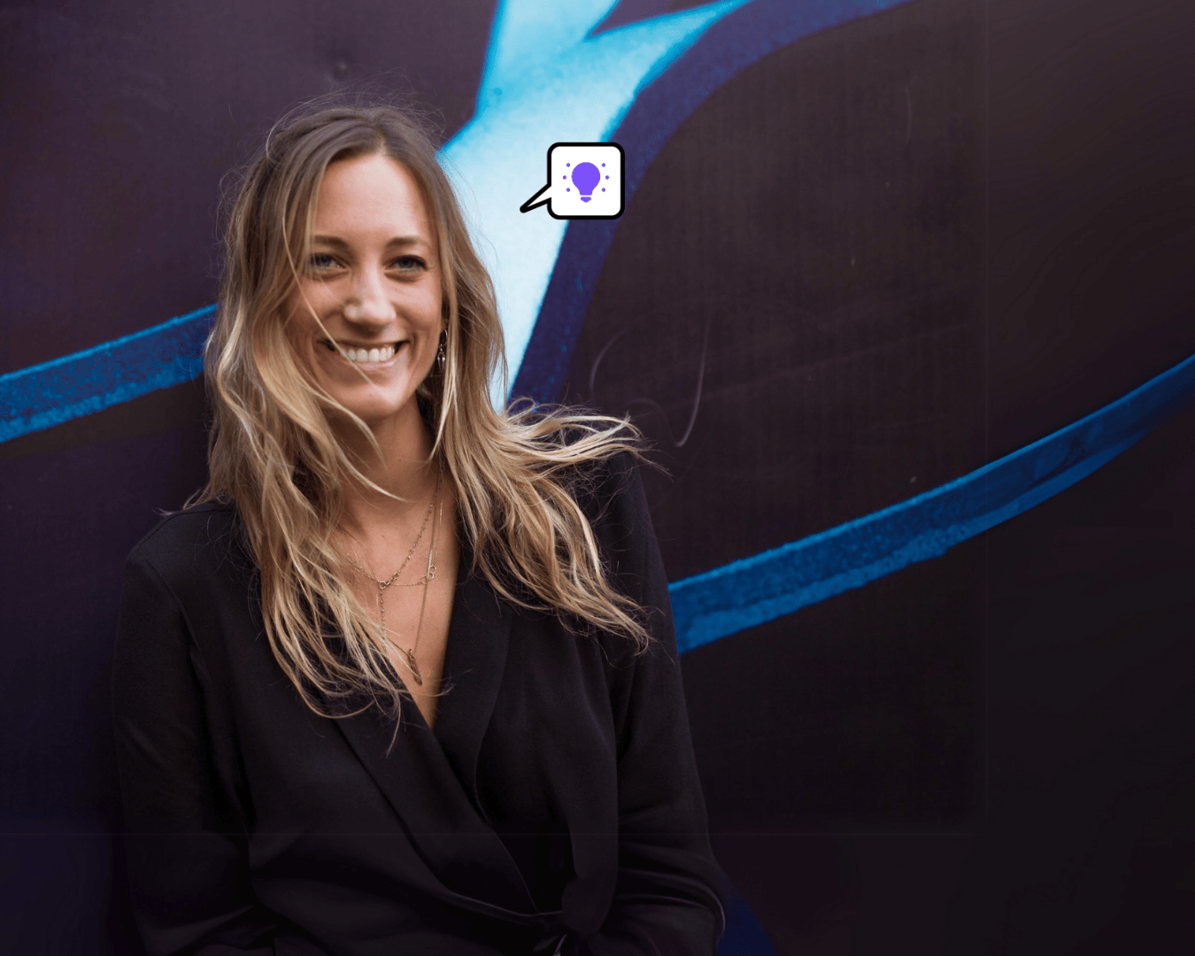 Blonde woman in black wrap blazer smiles confidently against a dark mural, representing Wiser employee advocacy and personal authenticity.