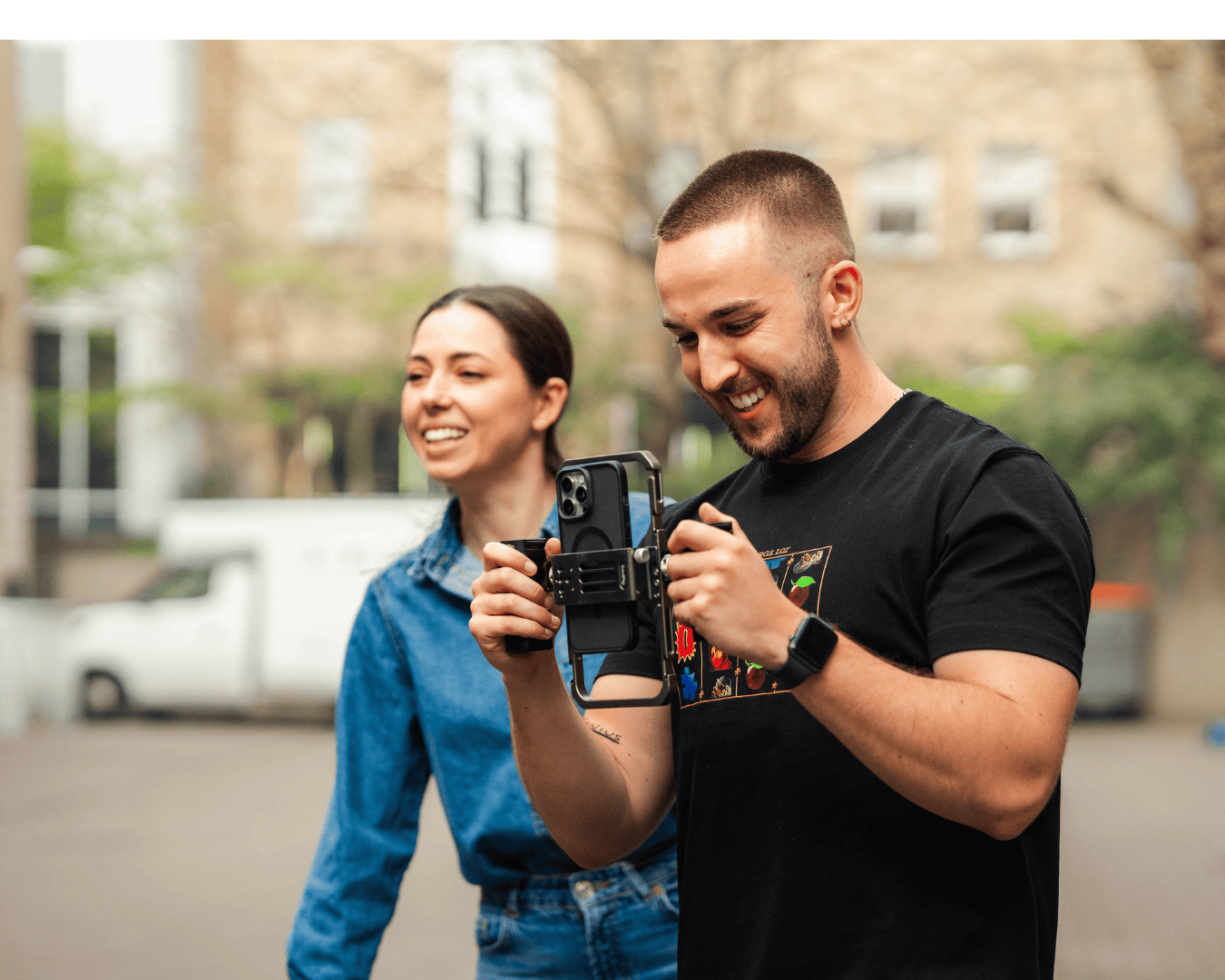 Young man films with smartphone rig while smiling woman watches, capturing behind-the-scenes content for employee advocacy storytelling campaign.