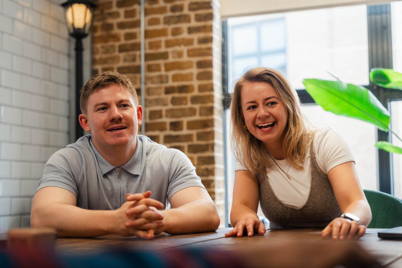 A white man with short hair and a white woman with blonde hair laugh during a meeting. They reflect DNV’s employee advocacy programme and its impact on workplace culture.