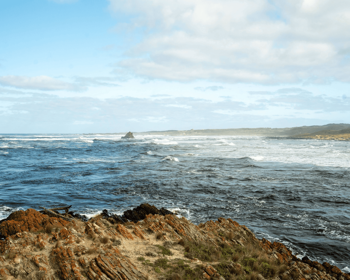 Wide shot of rugged rocks and crashing waves along the Tasman coast under blue skies. Establishing shot for employer brand video strategy tied to regional pride and place.