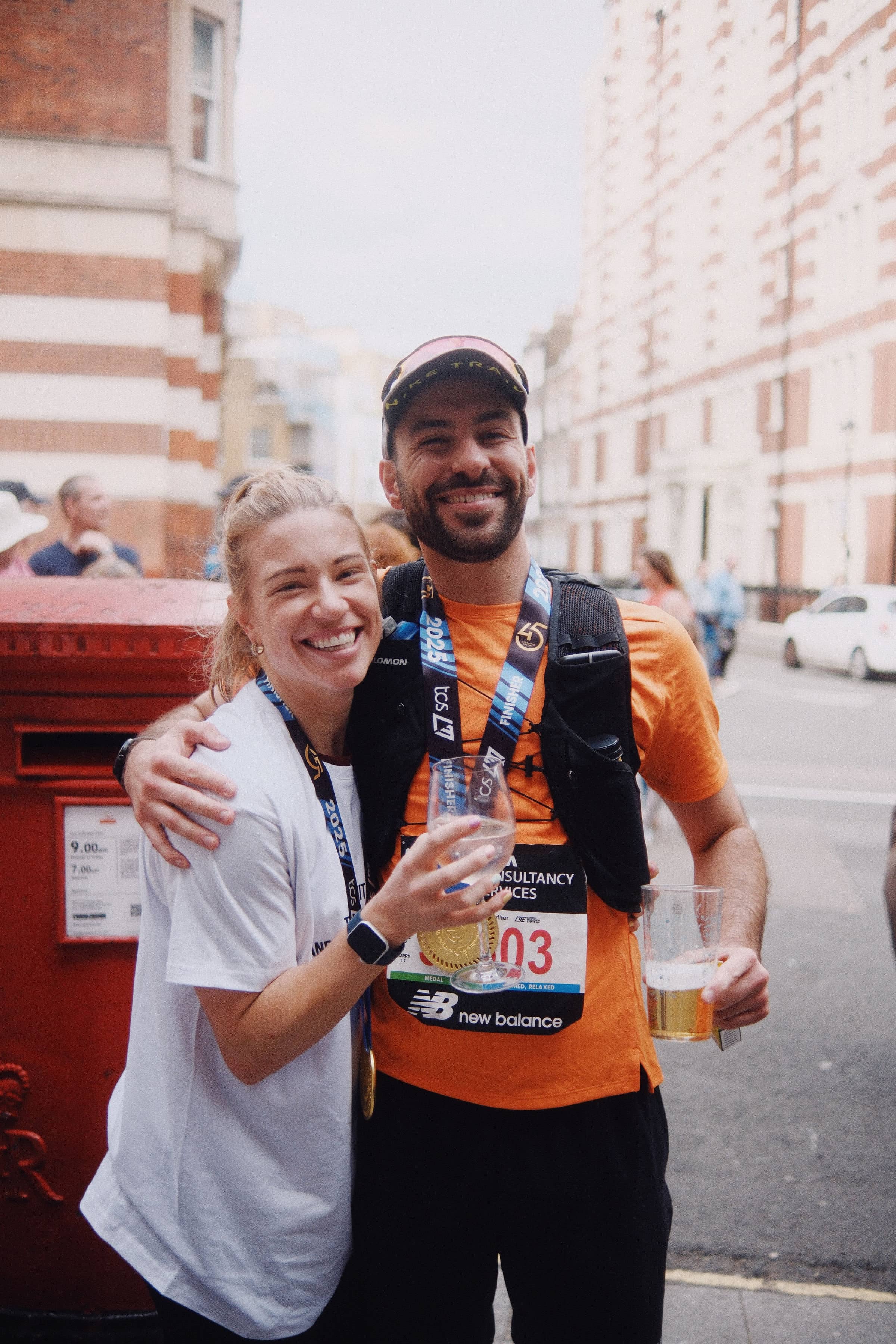 A white woman and man in running gear celebrate post-race, each wearing medals and holding drinks while embracing — capturing team spirit and resilience aligned with values-led company culture transformation.