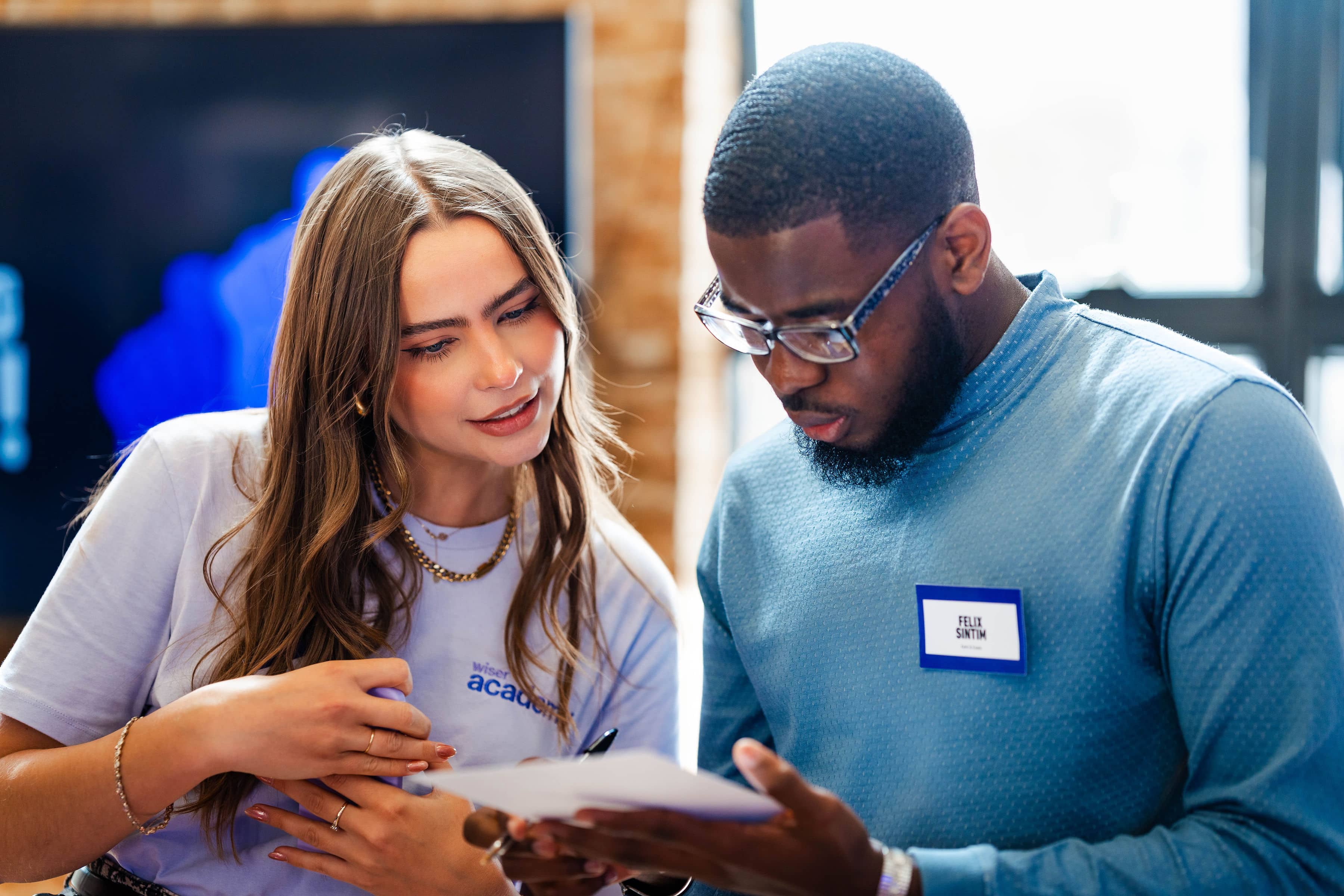 Young woman with long brown hair and gold jewellery speaks to a Black male graduate wearing glasses during an ambassador-led early careers training workshop.