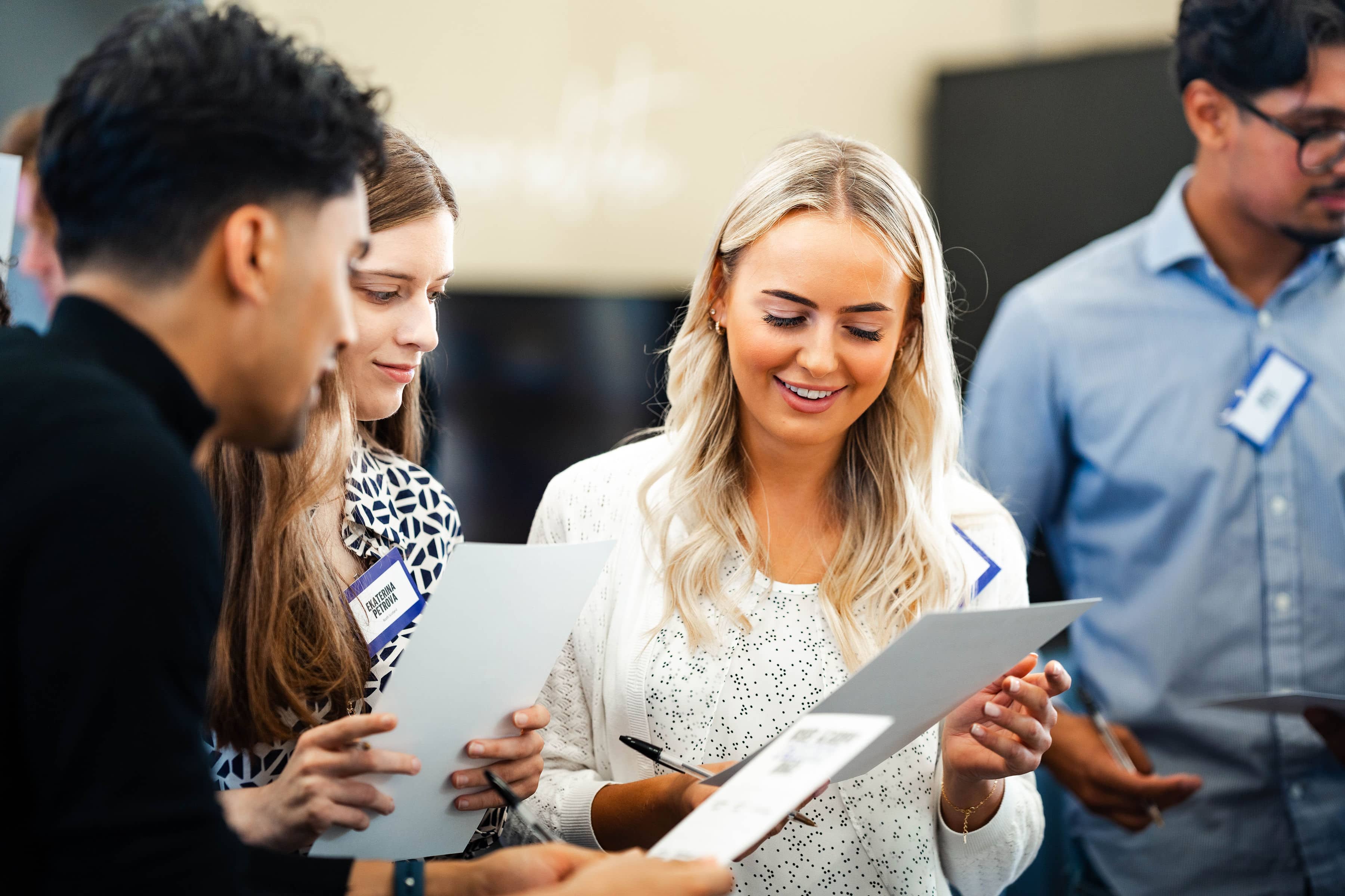 A group of early career graduates, including two women and one man of varying ethnicities, reviewing paperwork during a professional development training workshop indoors.