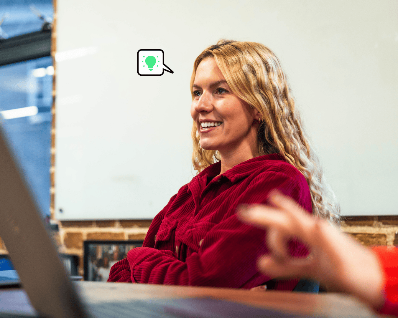 Photo of blonde female wearing a red top smiling in a meeting room with a whiteboard behind her