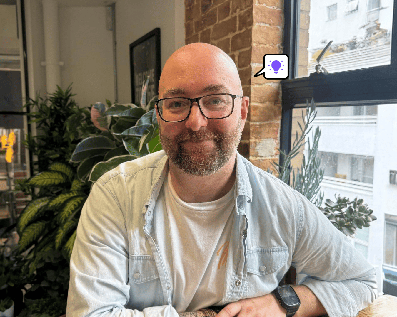 Photo of man with glasses in a shirt smiling with plants behind