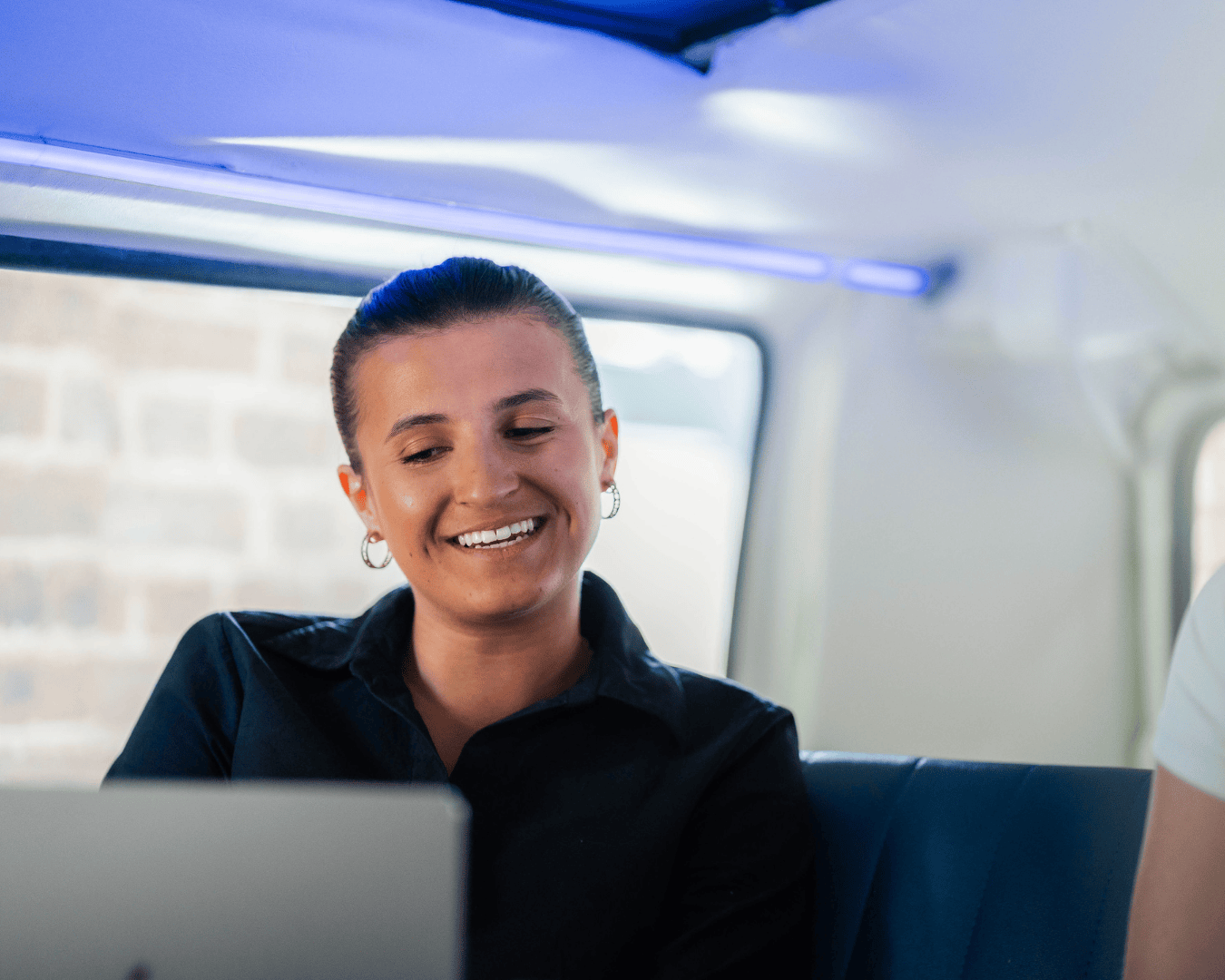 Photo of a female with brown hair and black top smiling and looking at a laptop