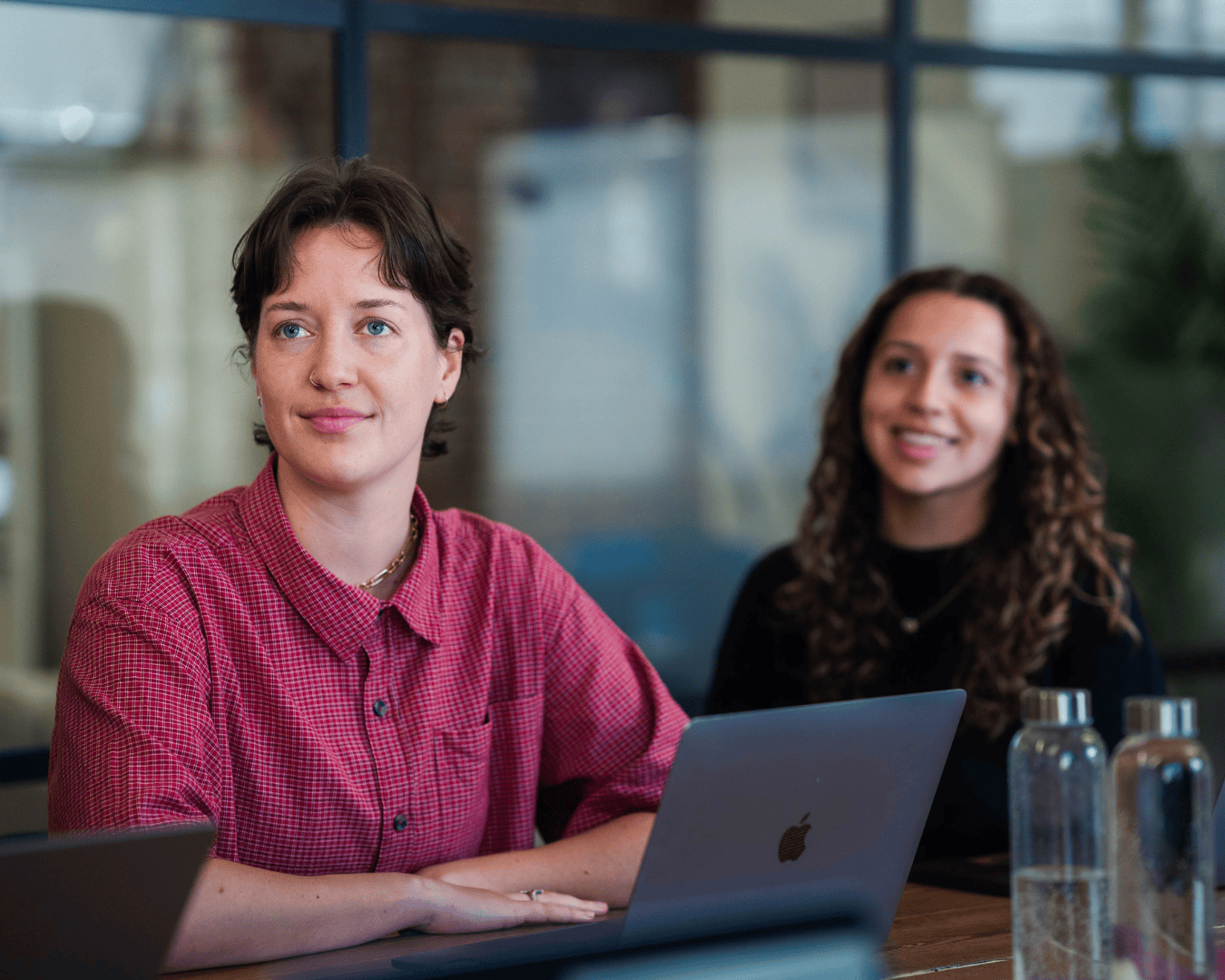 photo of two females with brown hair watching a presentation. One is in a red shirt the other a black jumper