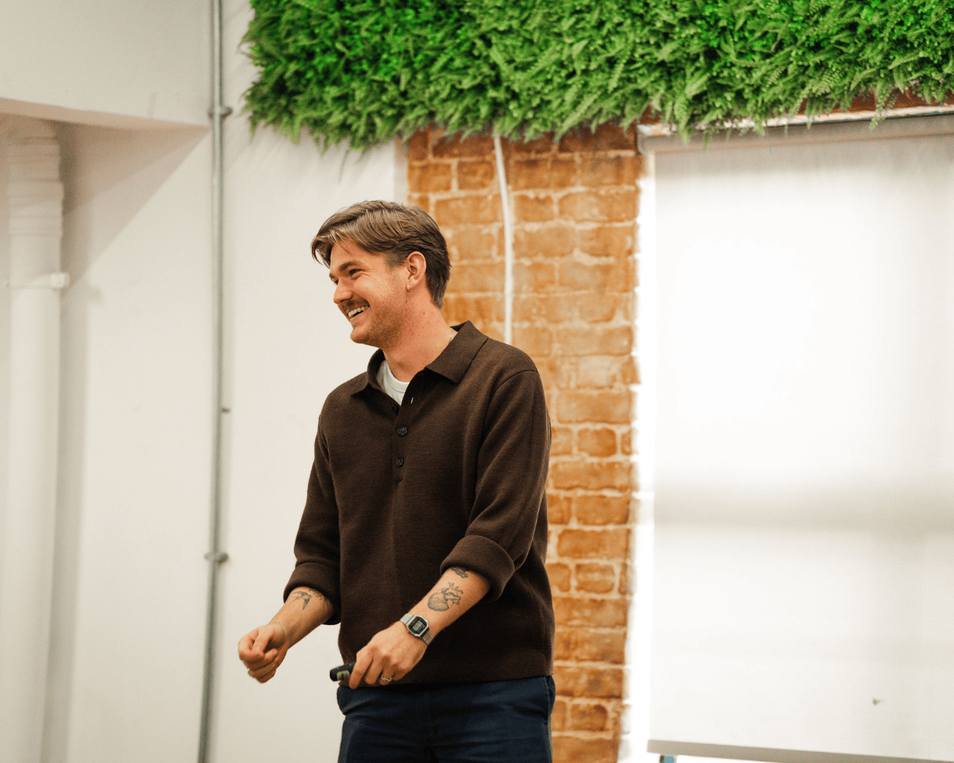 Photo of a man in a brown jumper with brown hair smiling standing on a stage