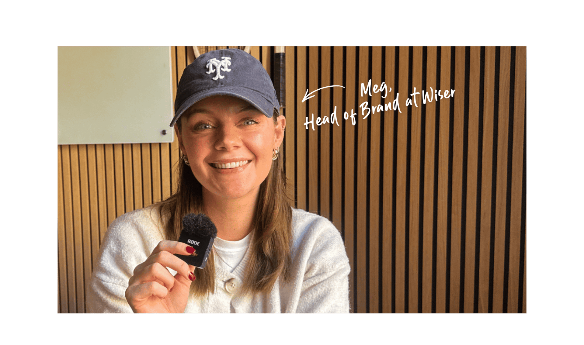 A smiling woman in a casual sweater and cap holds a small microphone. She sits in front of a wood-paneled wall. Text reads "Meg, Head of Brand at Wiser."