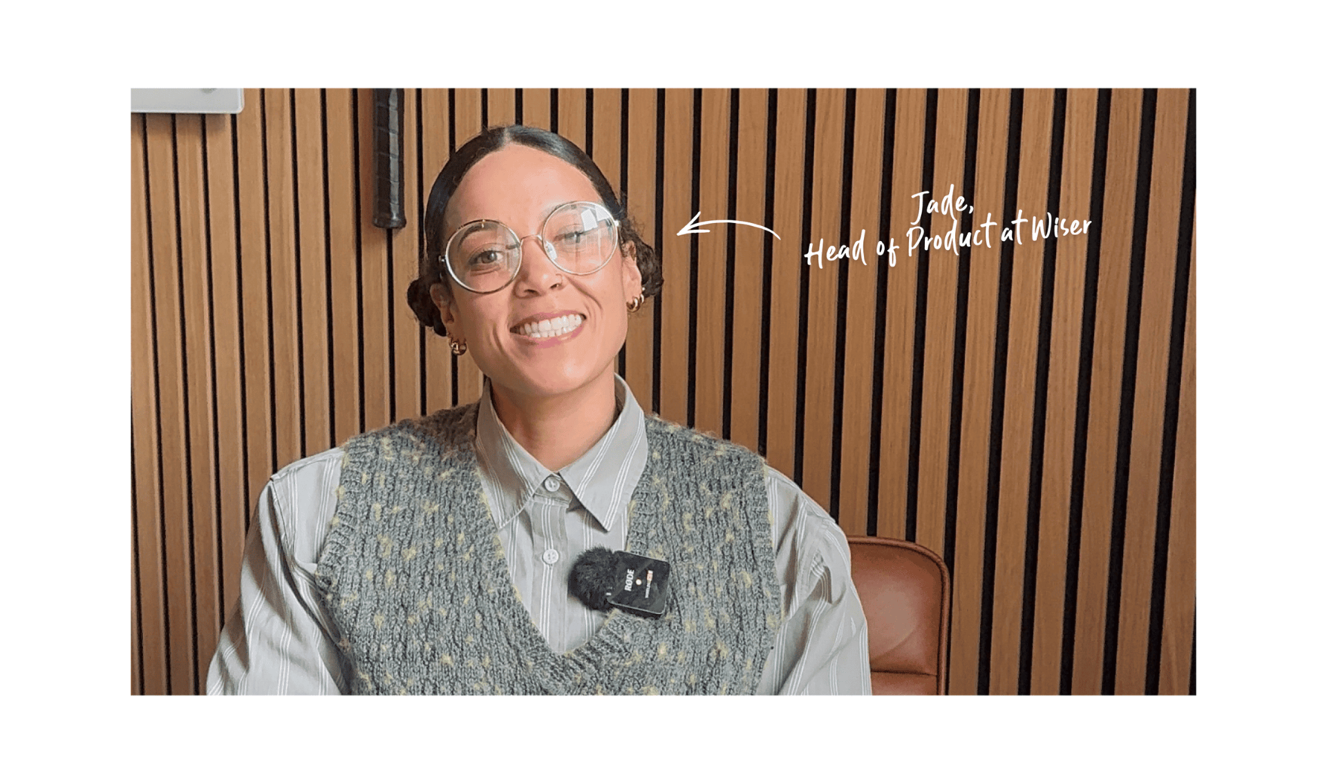 A smiling person with glasses and braided hair, sitting indoors against a wooden panel wall. They wear a gray shirt and vest with a microphone clipped on. The caption reads, "Jade, Head of Product at Wiser,.