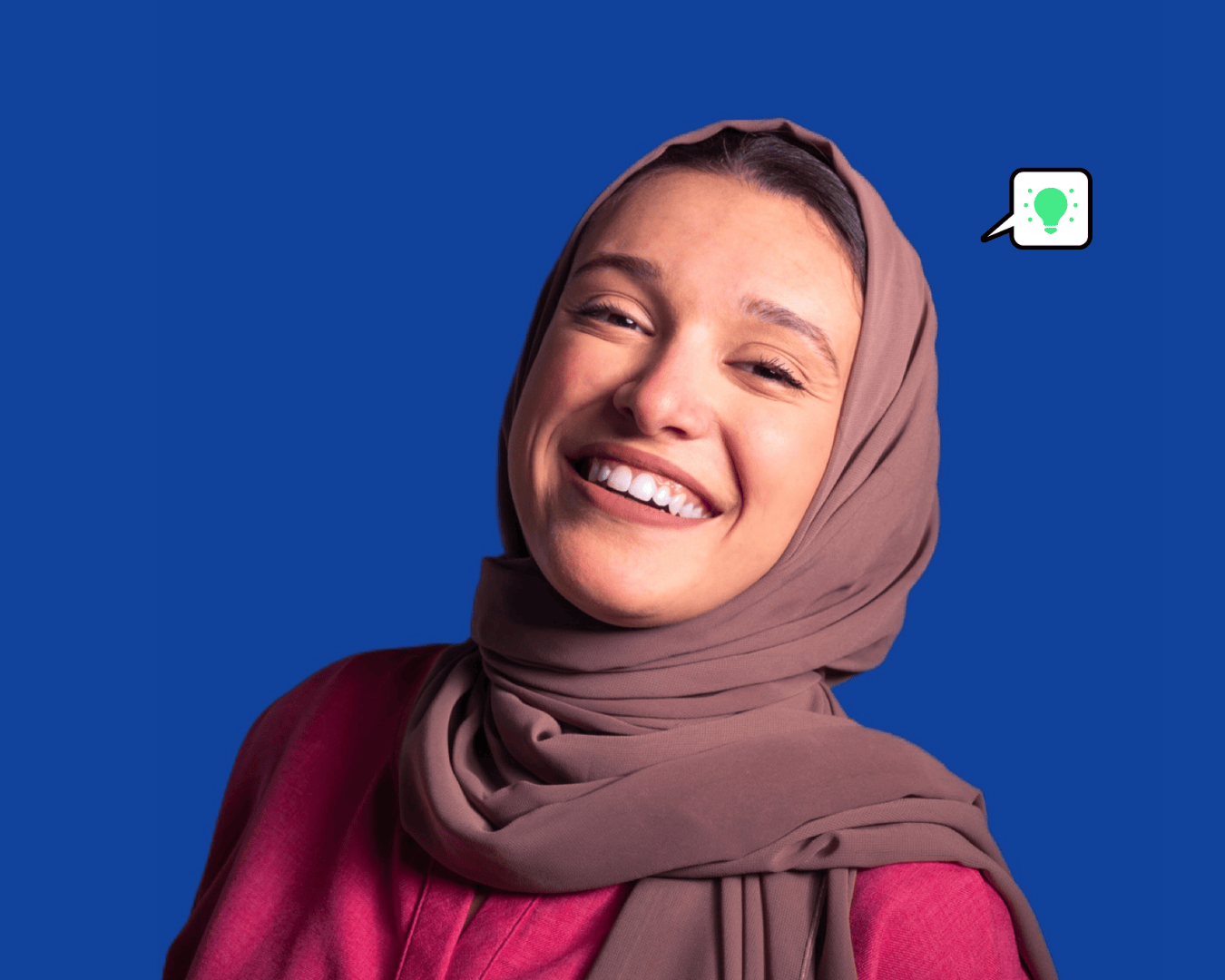A person in a brown head scarf and red top smiling warmly, set against a blue background. A small speech bubble with a light bulb icon is nearby