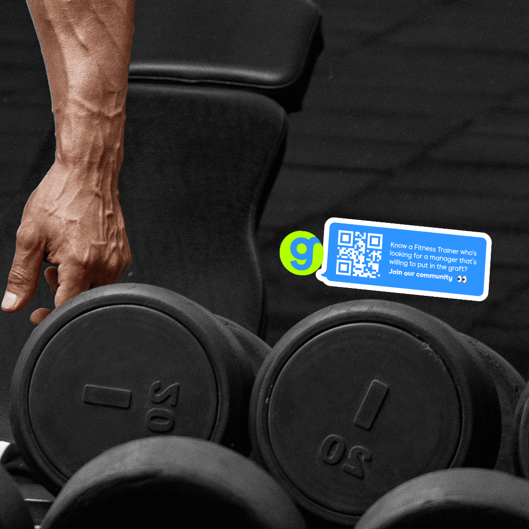 Close-up of black gym dumbbells on a rack with a branded sticker featuring a QR code. The sticker invites fitness trainers to join a community, linking physical gym equipment with digital recruitment through scannable, eye-catching design.