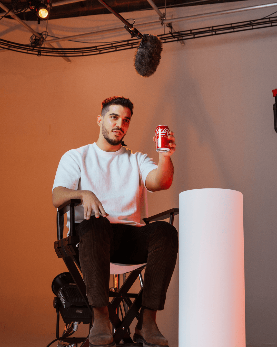photo of man in white t-shirt sat in a directors chair holding a coca-cola can