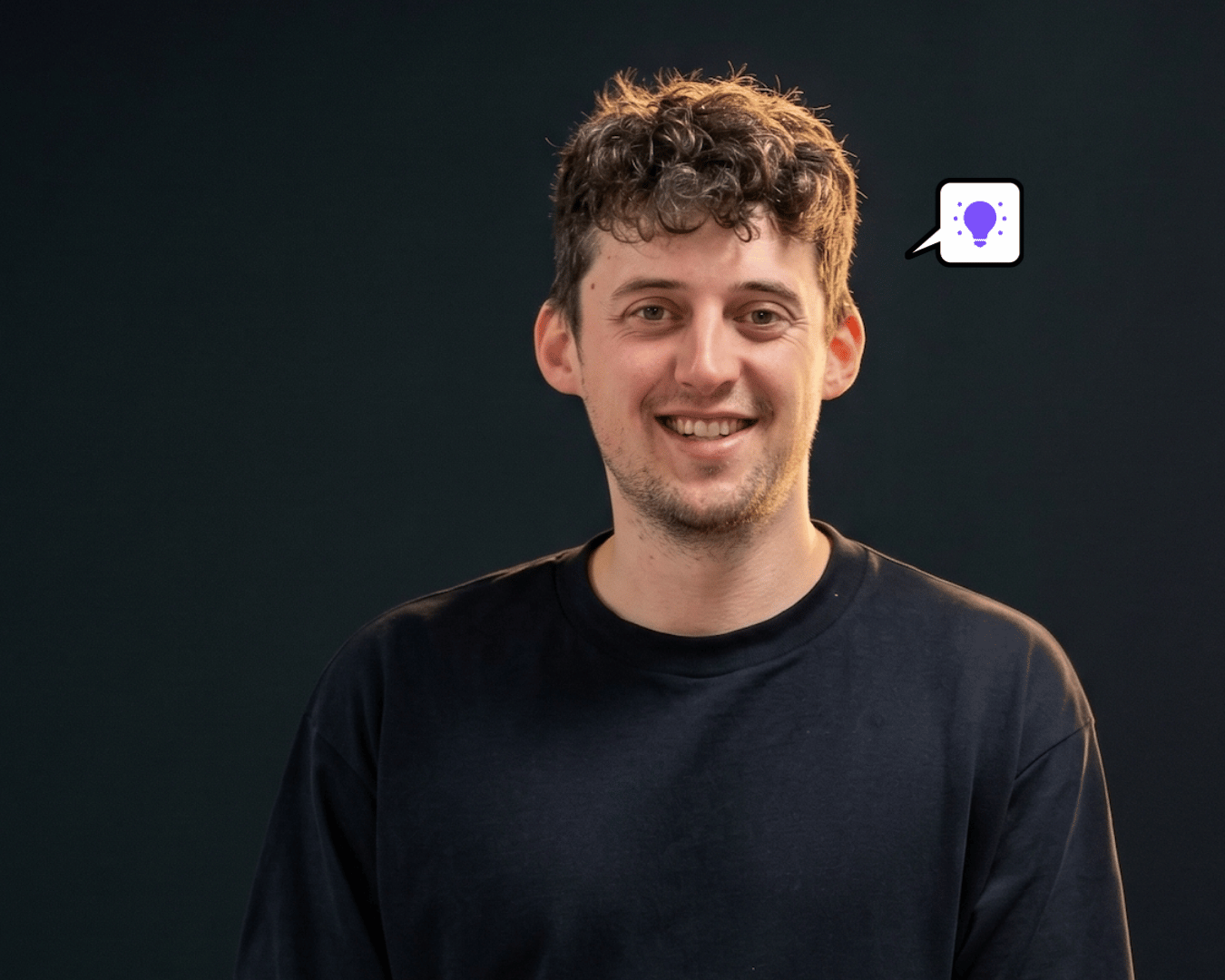 Smiling young man with short curly hair wearing a dark shirt against a dark background. A speech bubble with a purple light bulb is above his head.