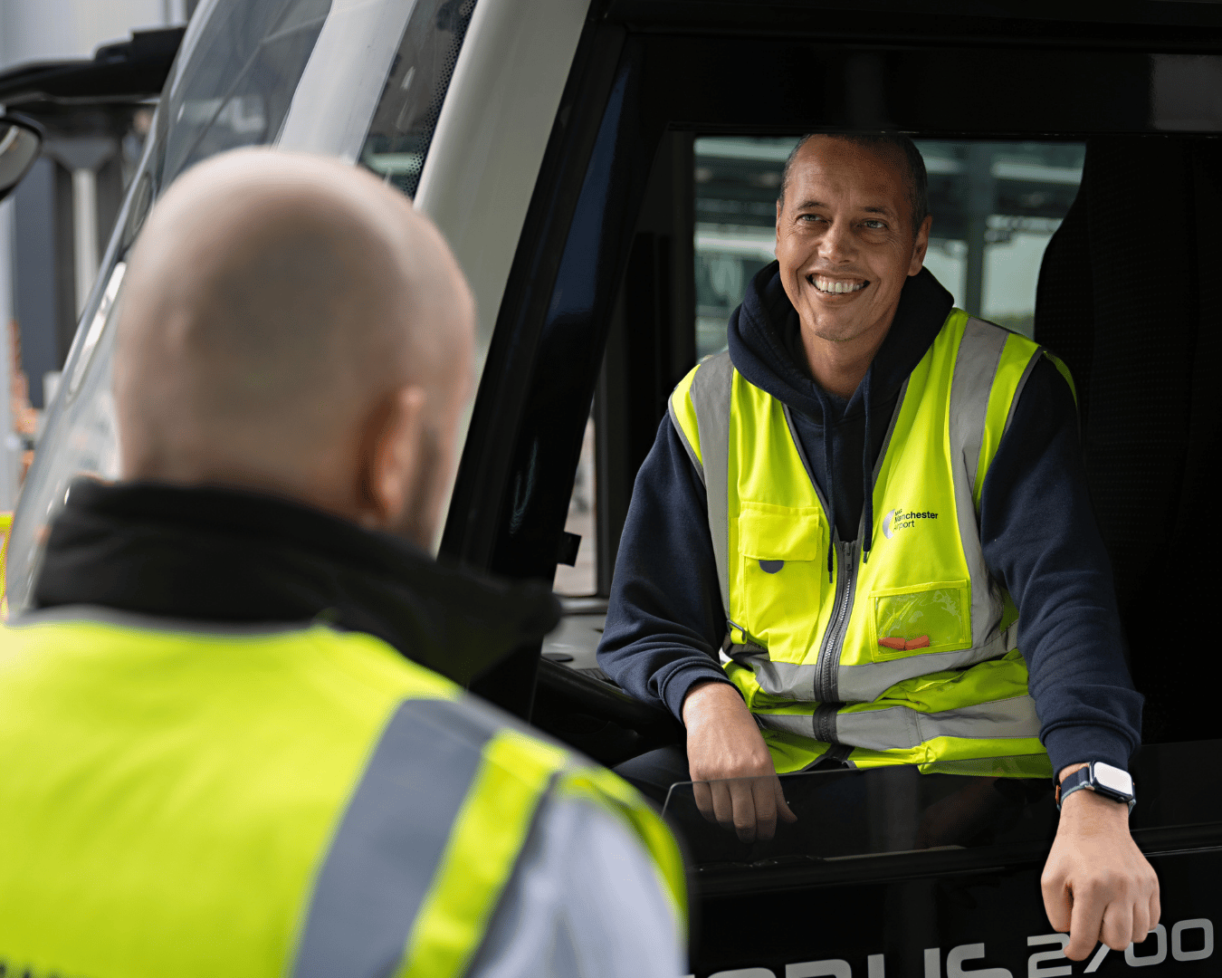 Smiling worker in a high-visibility vest sits in a bus