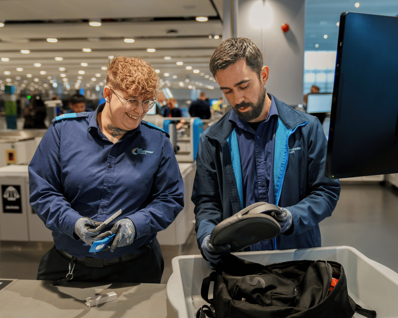 Two airport security officers inspect a luggage item at a screening station.
