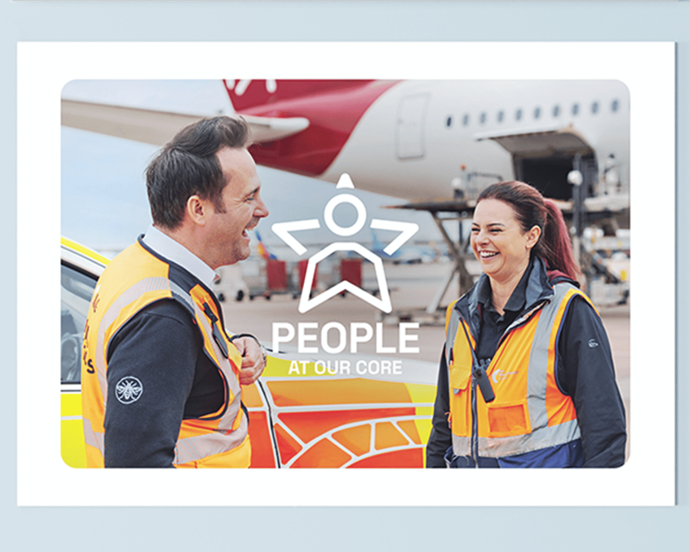 Two airport workers in safety vests, smiling and talking by an airplane. Text overlay reads "People at Our Core," conveying a friendly and positive atmosphere.