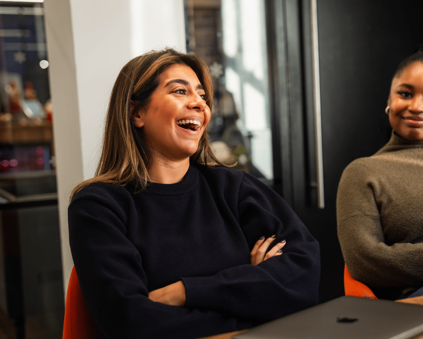Photo of female with brown hair laughing in a meeting wearing a black jumper
