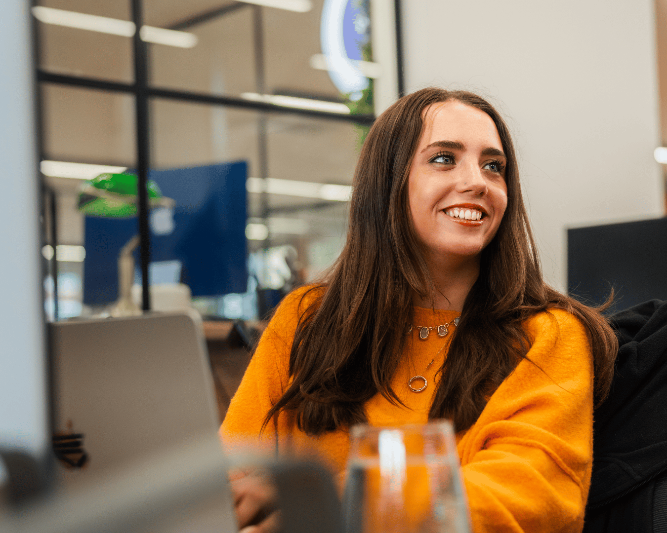 Female sat at desk smiling in and orange jumper
