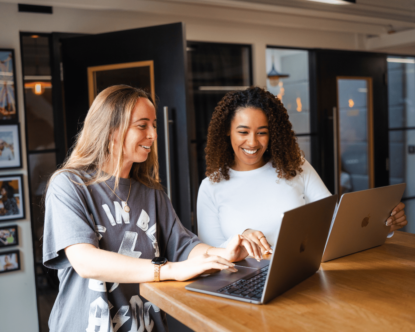 Two colleagues standing at a table and working together on laptops in a modern office environment.