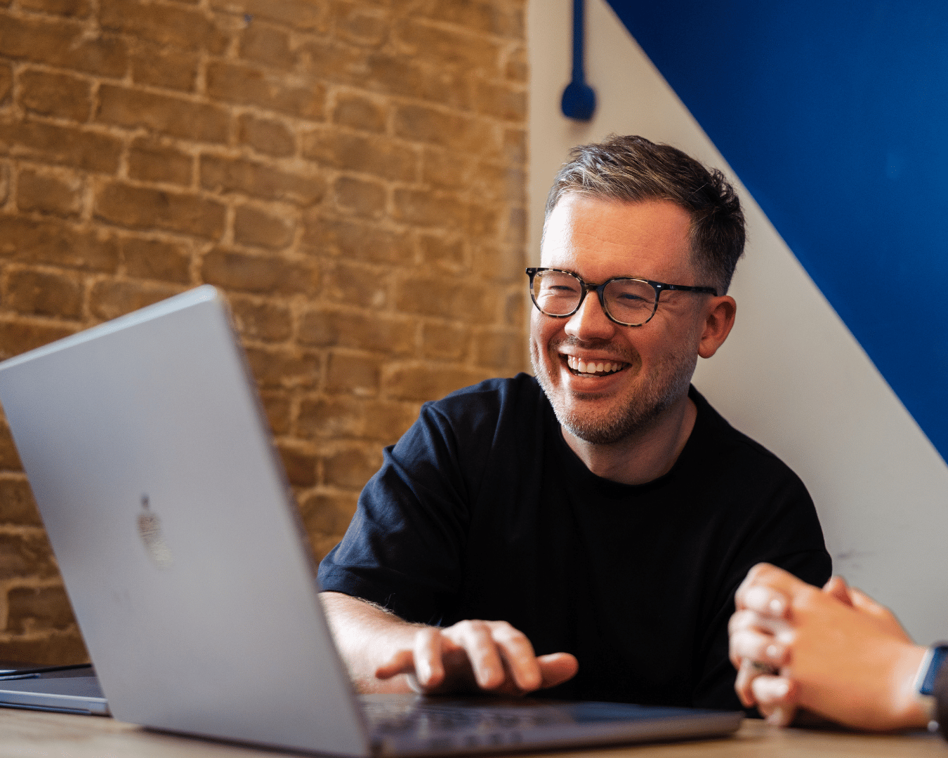 Employee collaborating on a laptop during a meeting in a modern office, smiling while discussing work with colleagues.