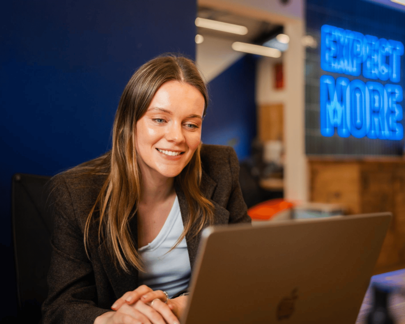 Photo of a female with brown hair in a green blazer looking at a laptop smiling