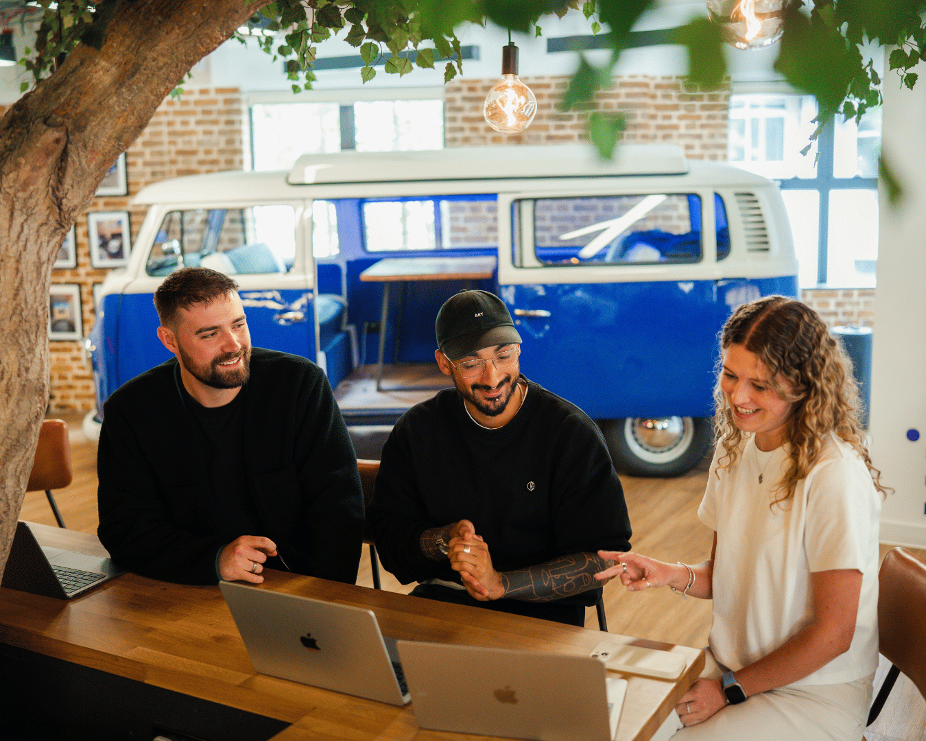 photo of two males and a female looking at a laptop screen in an office and smiling
