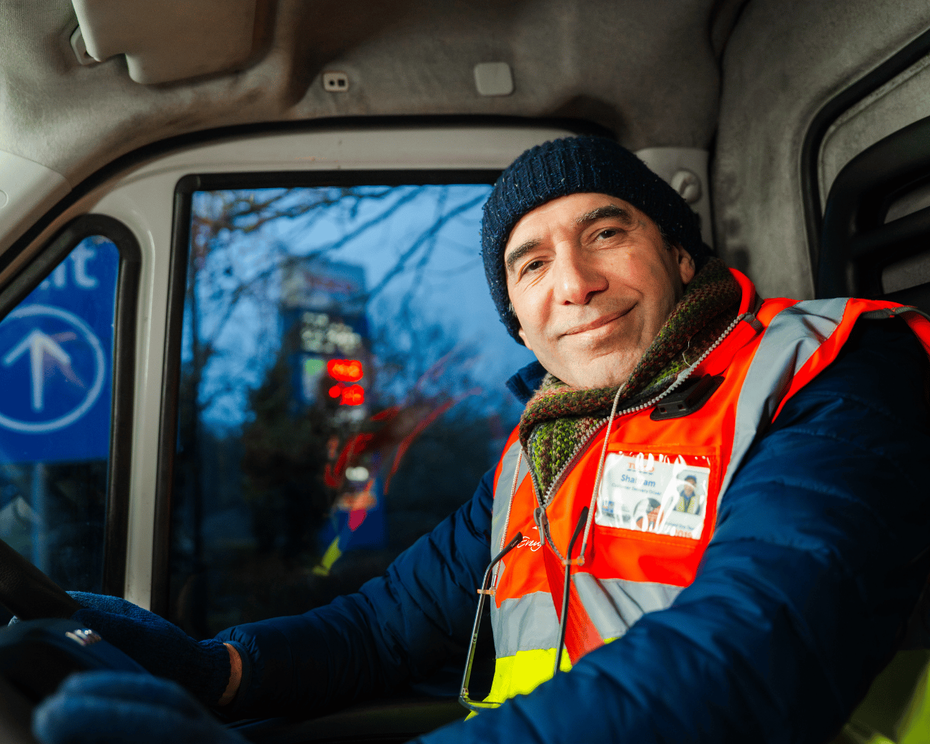 Photo of a man in a van wearing a hat and hi-vis jacket smiling