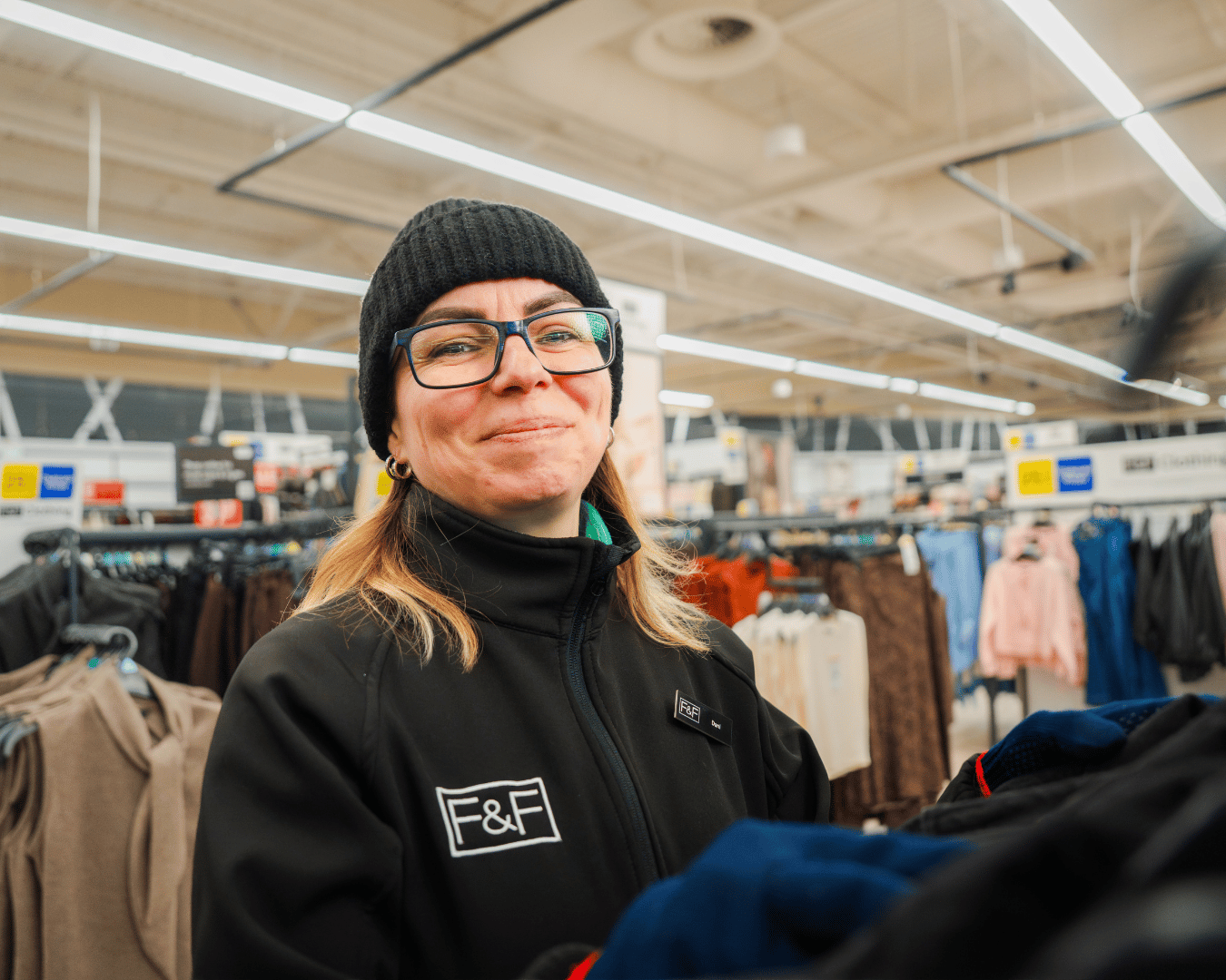 Female with blonde hair and glasses smiling at the camera in the clothes section of a supermarket