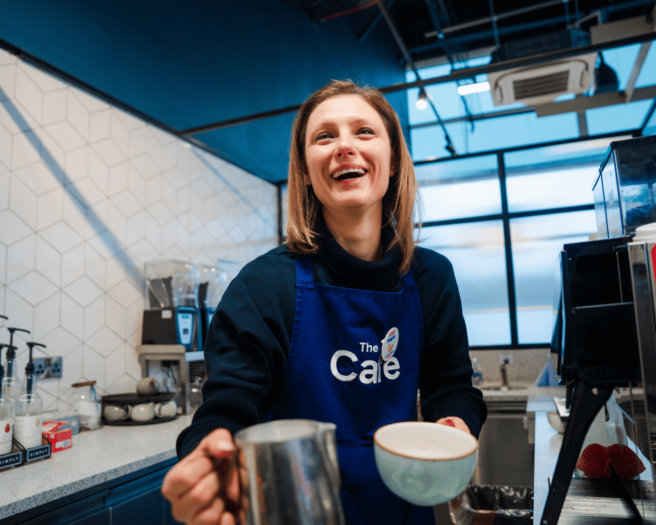 Photo of a female with brown hair smiling in a cafe making a coffee