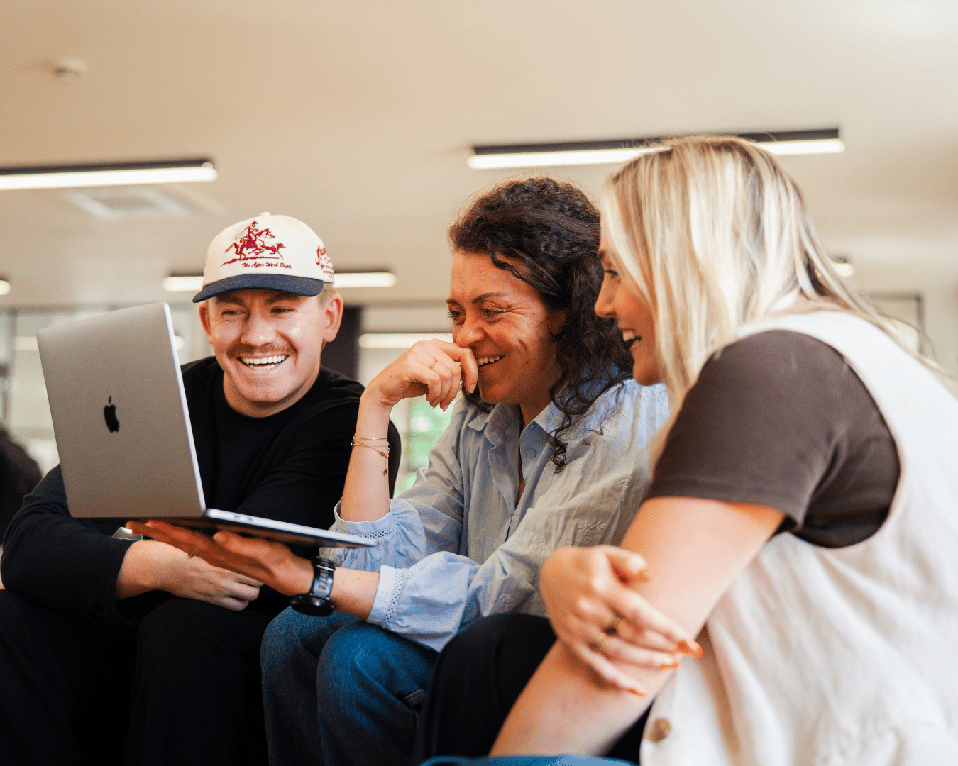 Three coworkers smile and laugh together while viewing a laptop in a bright office