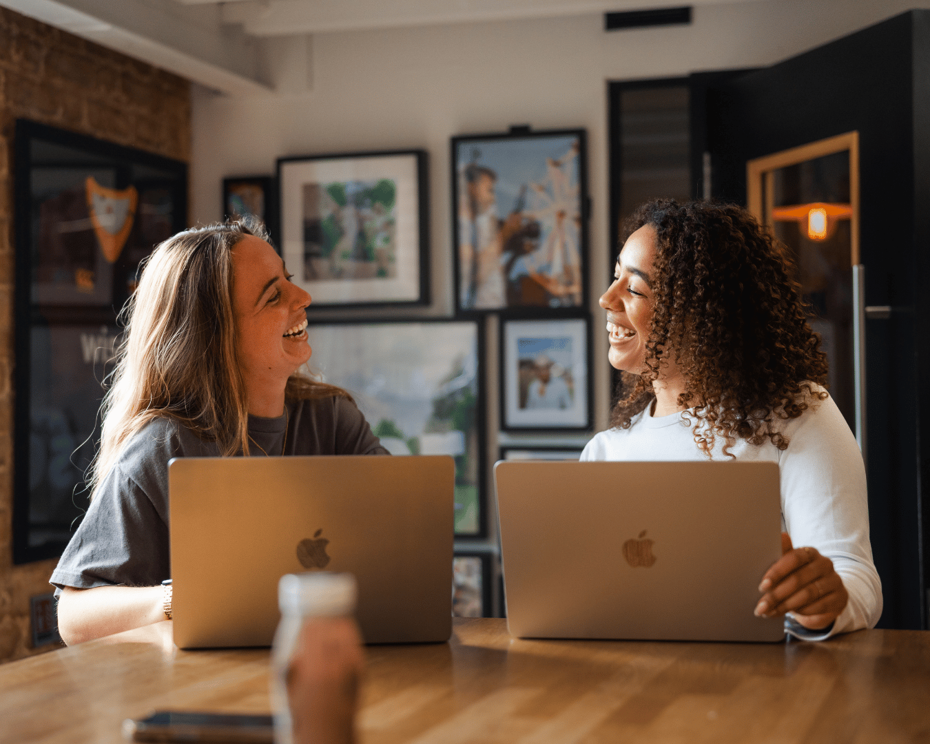 photo of two female in an office with laptops smiling at each other