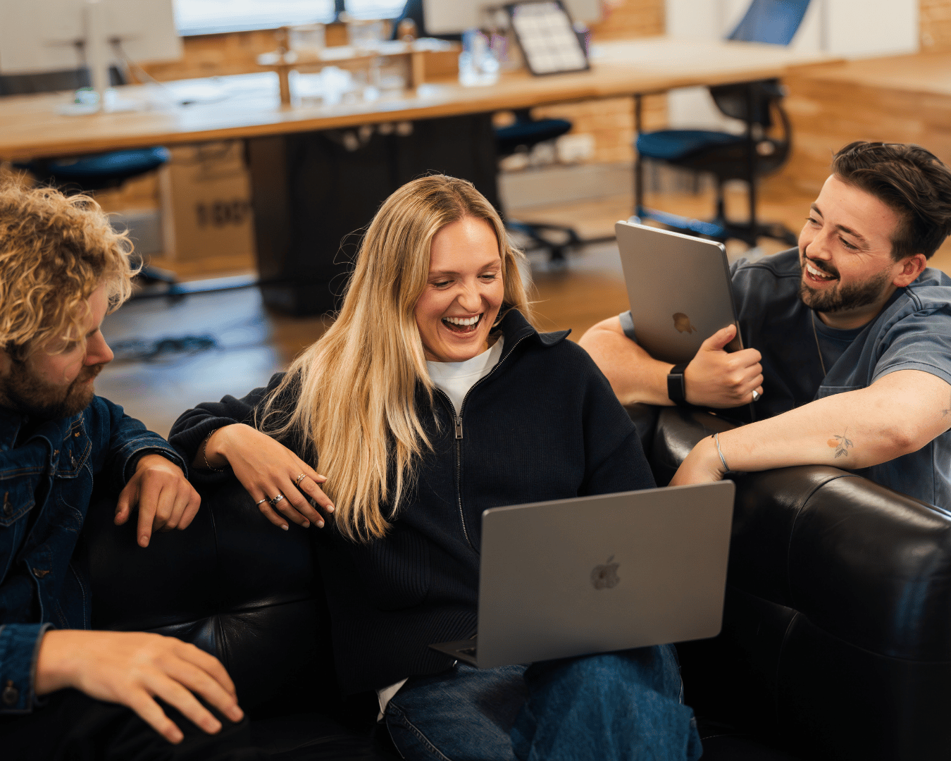 Photo of three people on a sofa smiling and looking at a laptopn