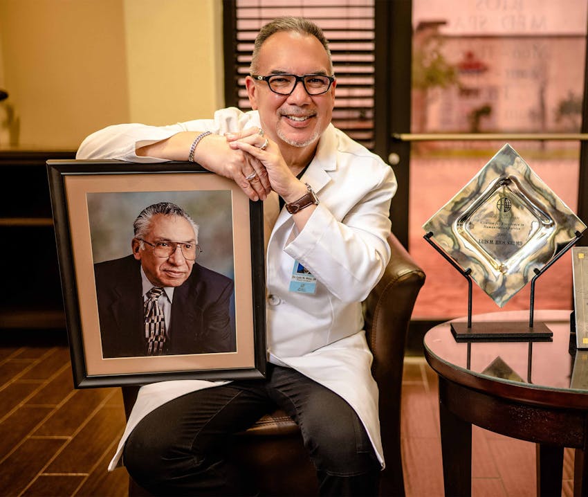 Dr. Rios next to awards and holding up picture of lost family member