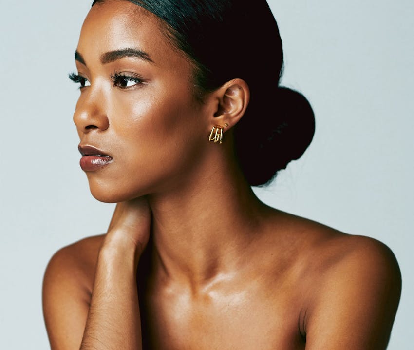 woman with bun with hand on her neck looking away from camera
