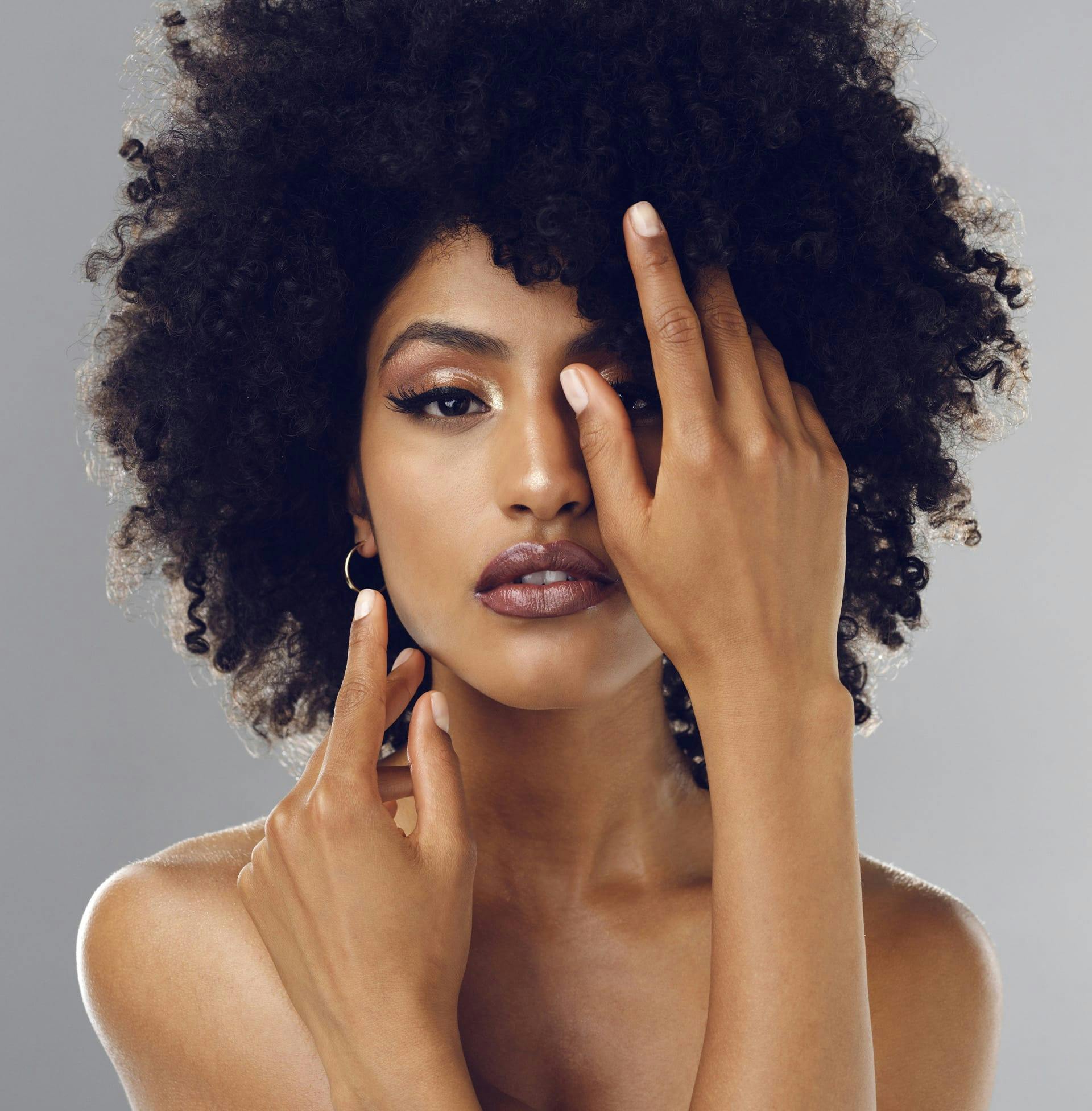 woman with afro covering one eye with her hand