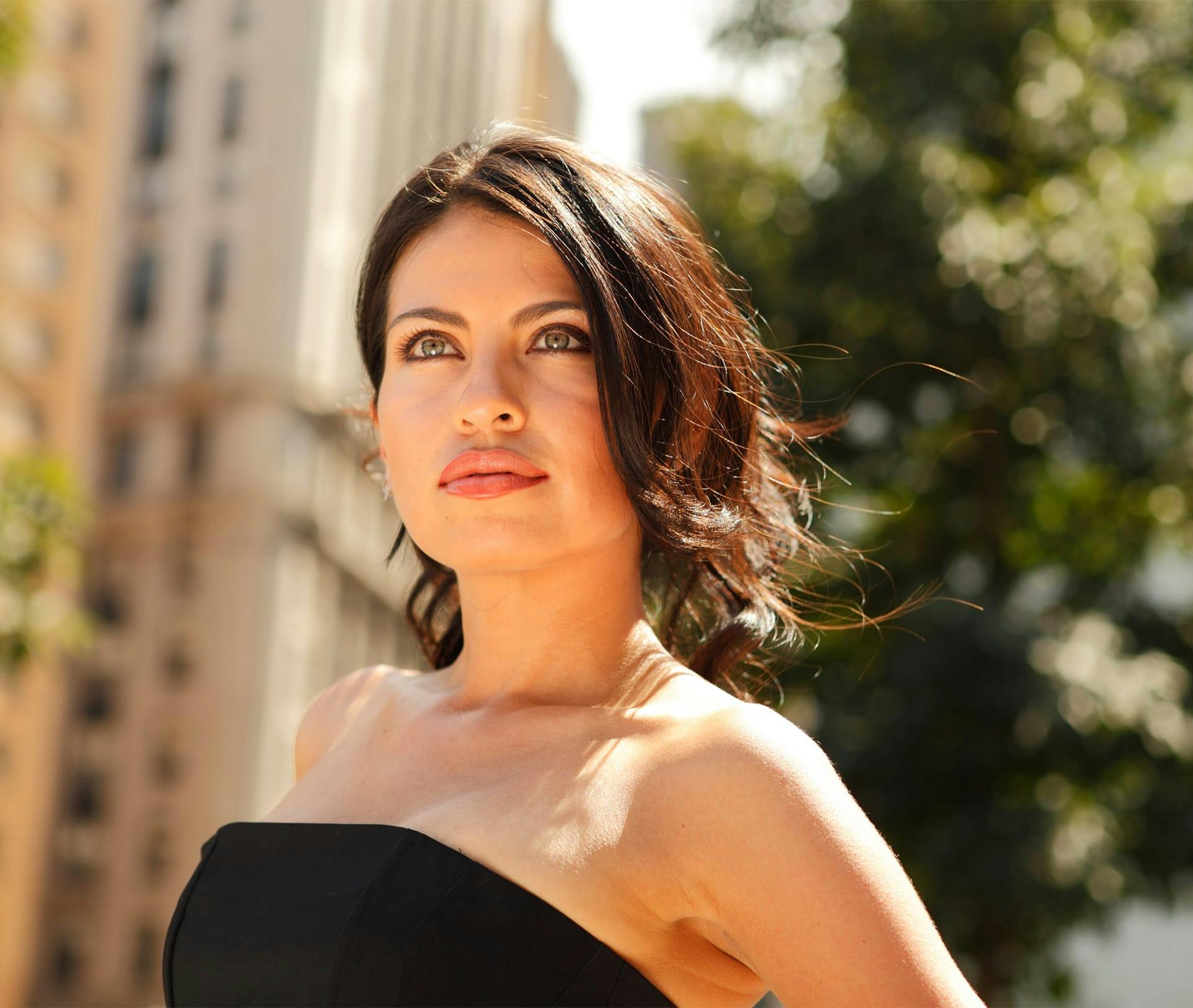 woman with short brown hair with buildings behind her