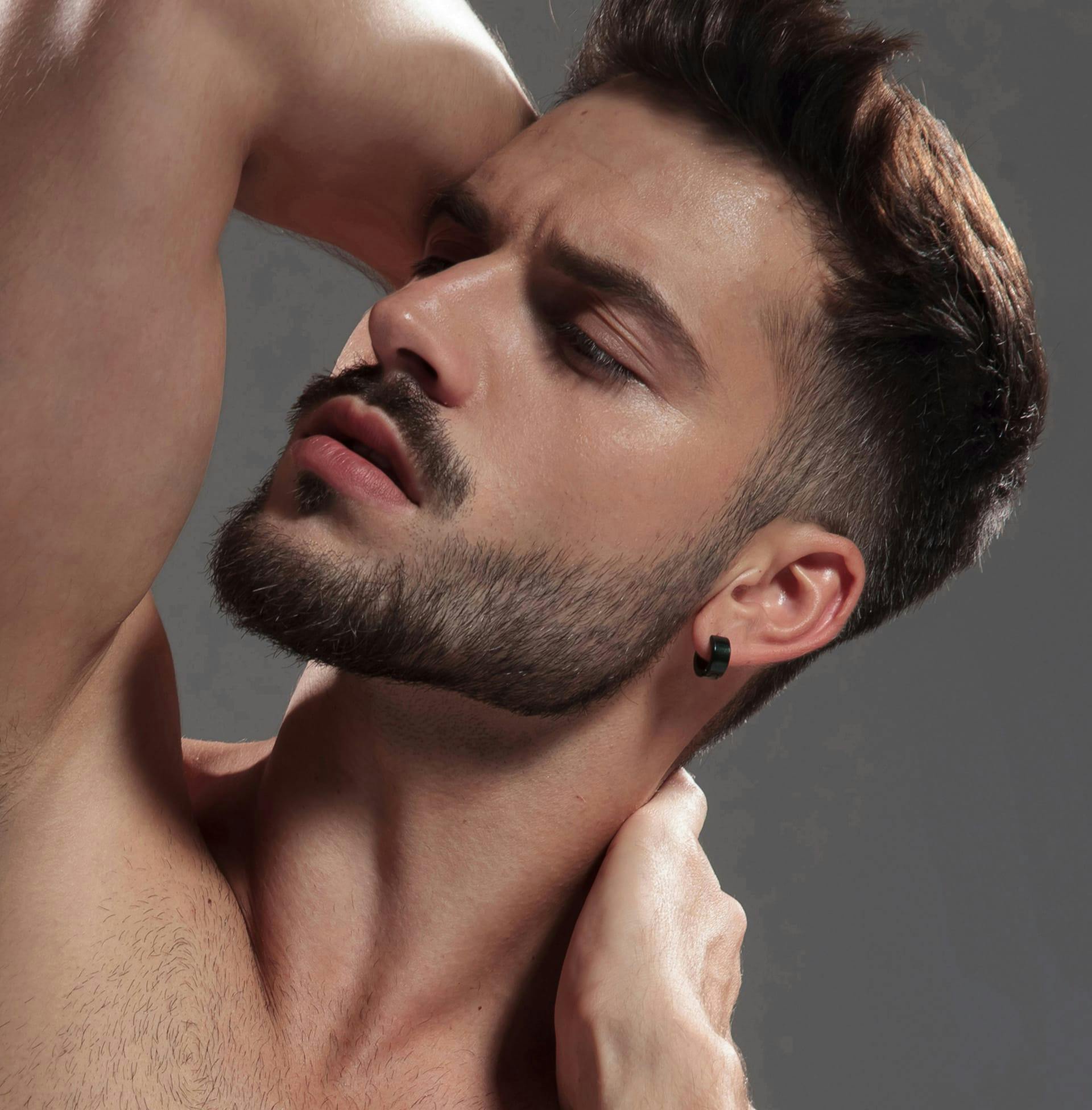 man posing with arms behind his head as he looks away from camera